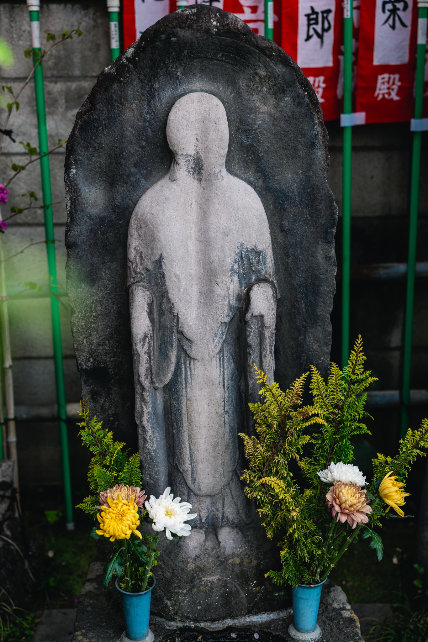 Heavily worn stone Kankan Jizō at Anyoin Temple in Senju, Tokyo, with its facial features almost completely gone and flowers placed before it.