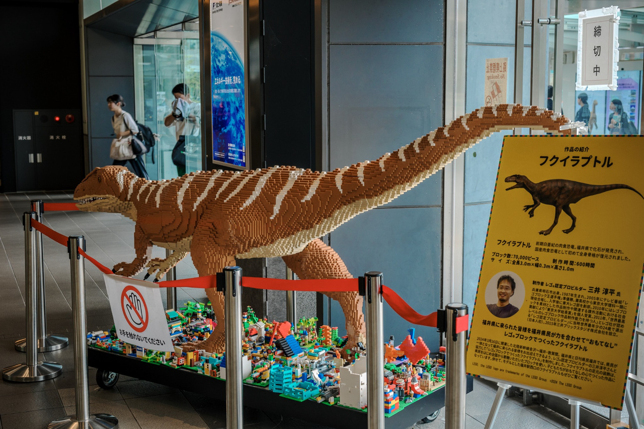 Three-metre Fukuiraptor model made from LEGO bricks, with a display panel and small LEGO-built scenes around its feet.