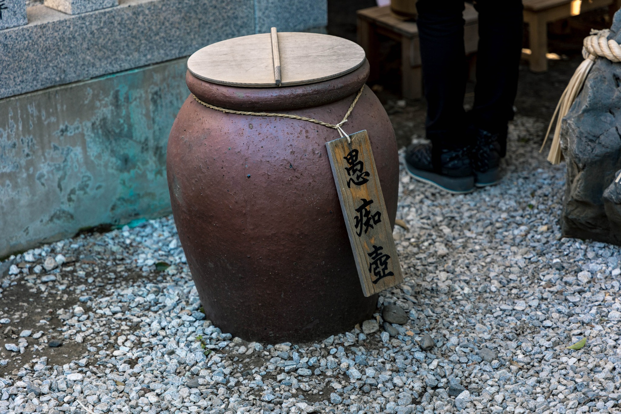 A large earthenware jar with a wooden lid and a sign reading guchitsubo.