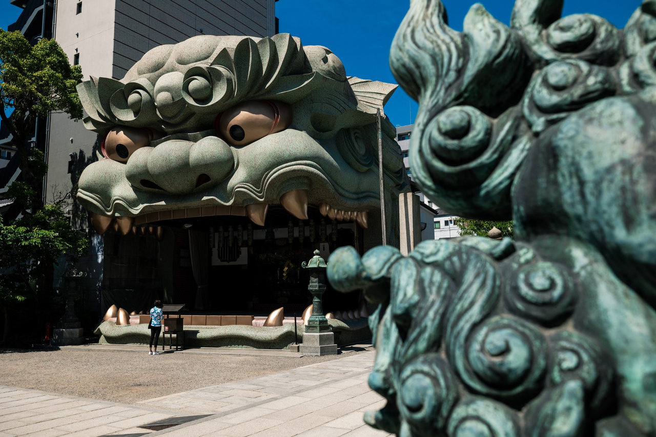 Stone komainu in the foreground with the much larger lion-head Shishi-den behind it at Namba Yasaka Shrine.