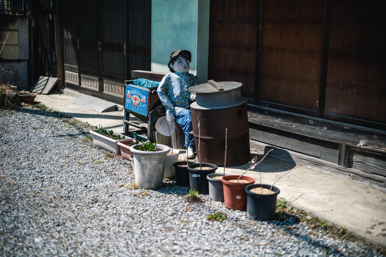 A handmade scarecrow sits beside a large cooking pot in Niegawa-juku.