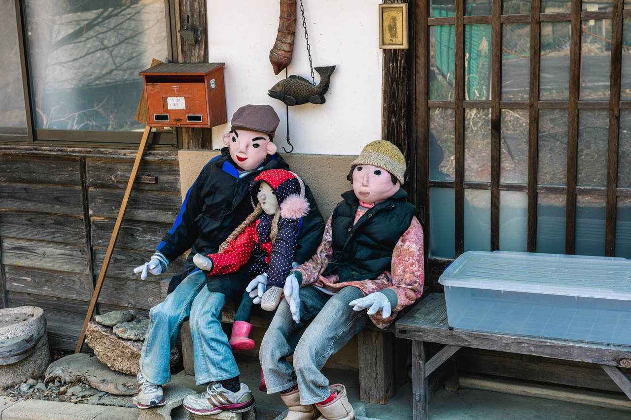 Three handmade scarecrows sit together outside a house in Niegawa-juku.