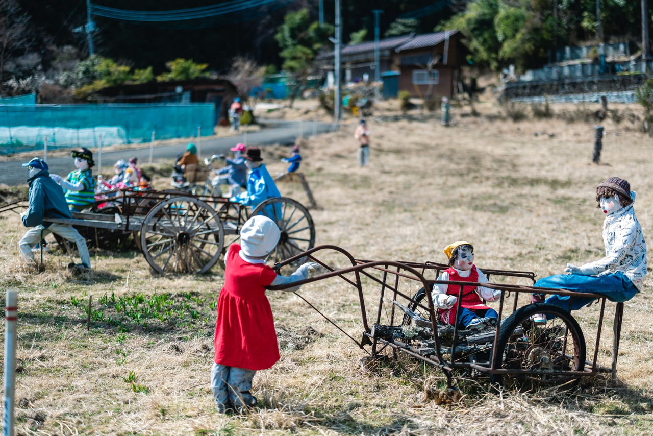 Handmade scarecrows gather around a handcart in an open area of Niegawa-juku.