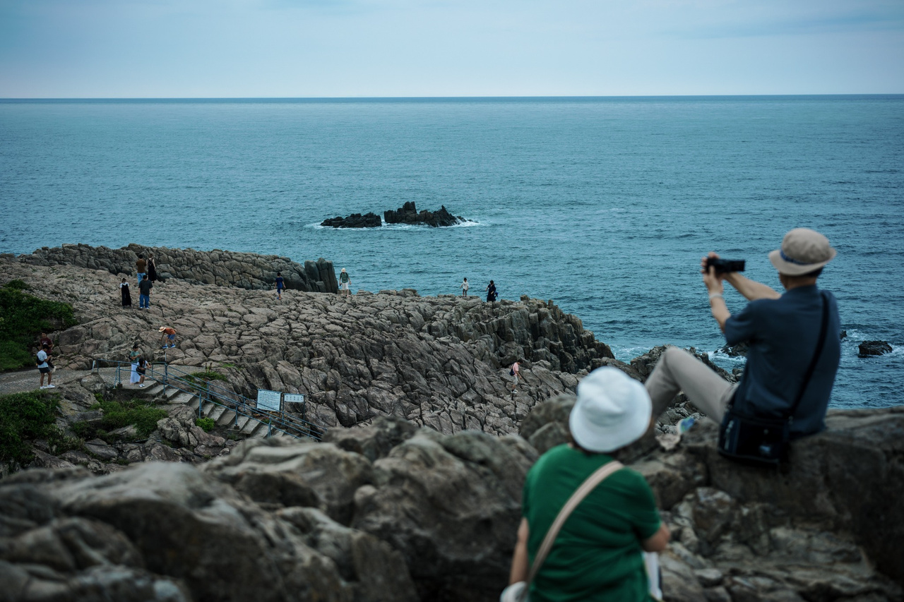 Visitors walking directly across the exposed rocks at Tojinbo, with the Sea of Japan beyond.