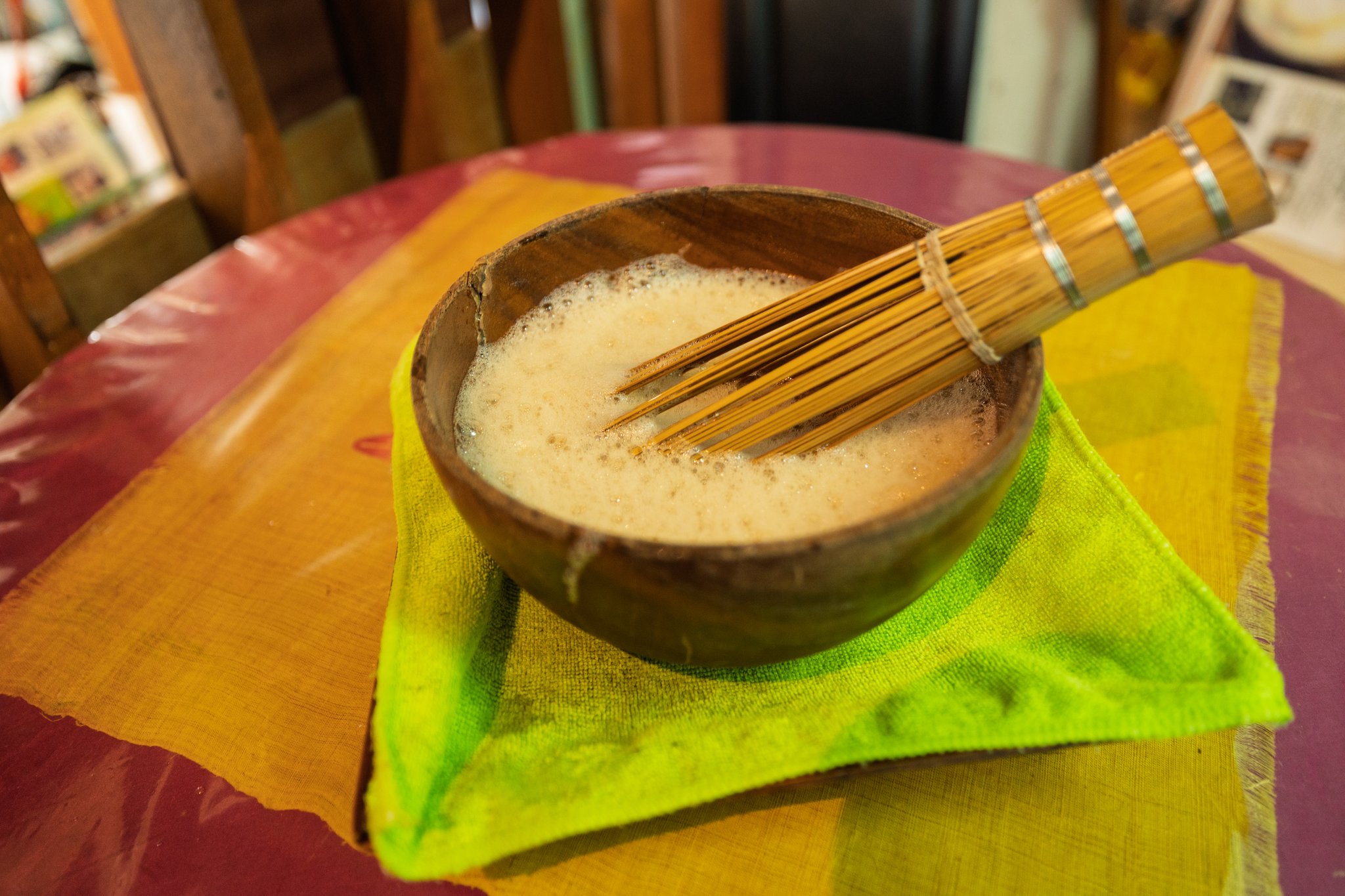 The same wooden bowl now covered with pale foam, the bamboo whisk resting in it