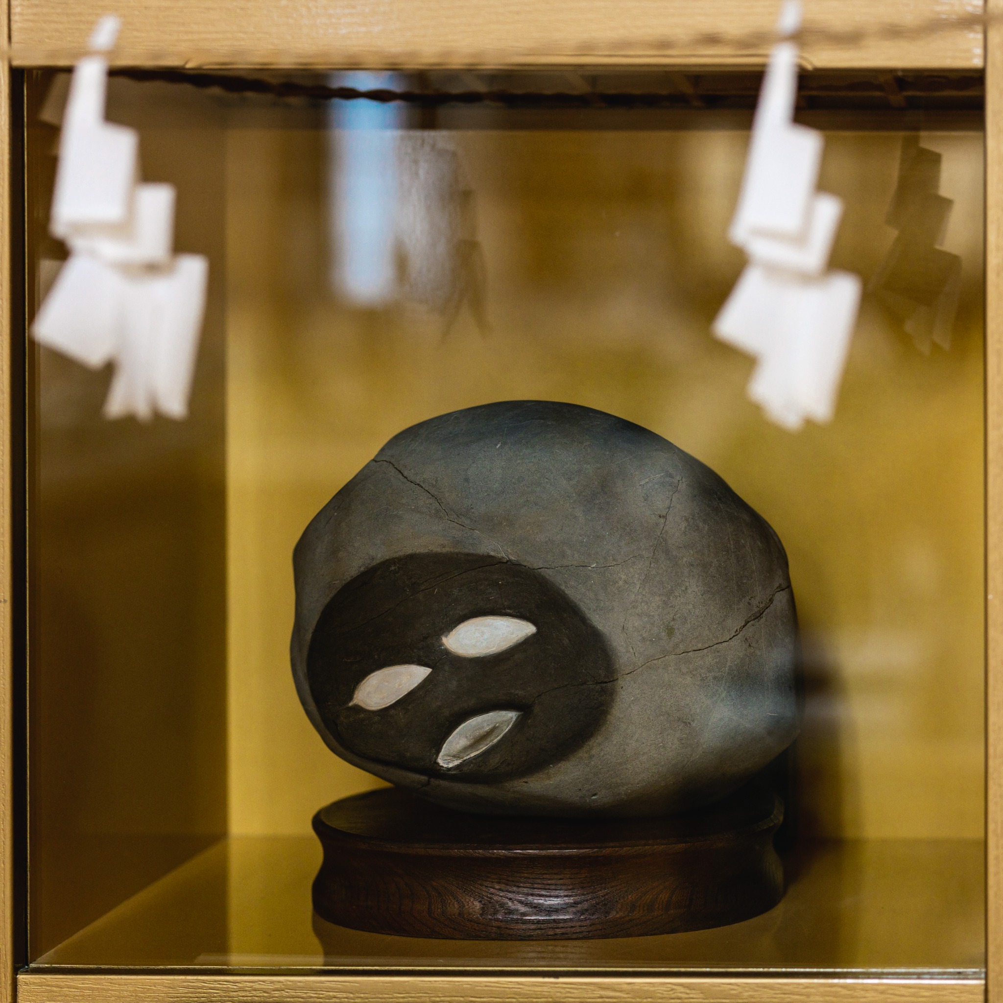 A rounded stone with pale shell fossils resembling eyes and a mouth, displayed in a gold-backed case at Chinsekikan.