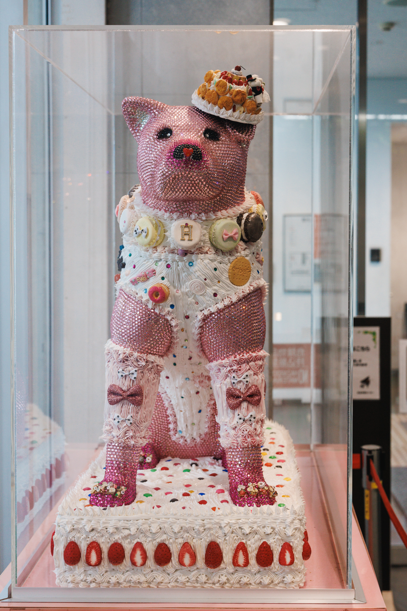 Front view of Deco Hachikō with a red heart-shaped nose, an H on its macaron collar and pink bows on its forelegs