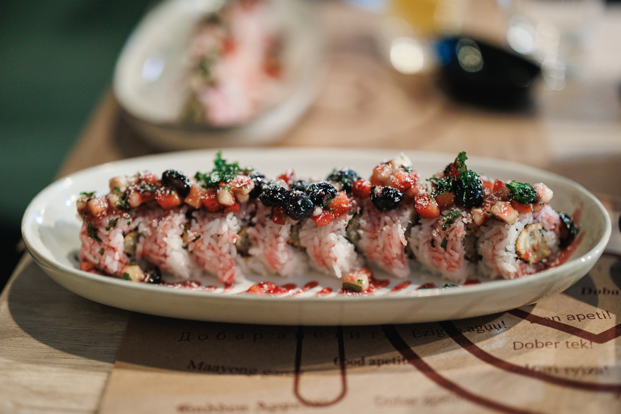 Dessert sushi rolls topped with berries and fruit, with fried banana, nori and rice visible in a cut end at Tokio Sushi in Novi Sad.