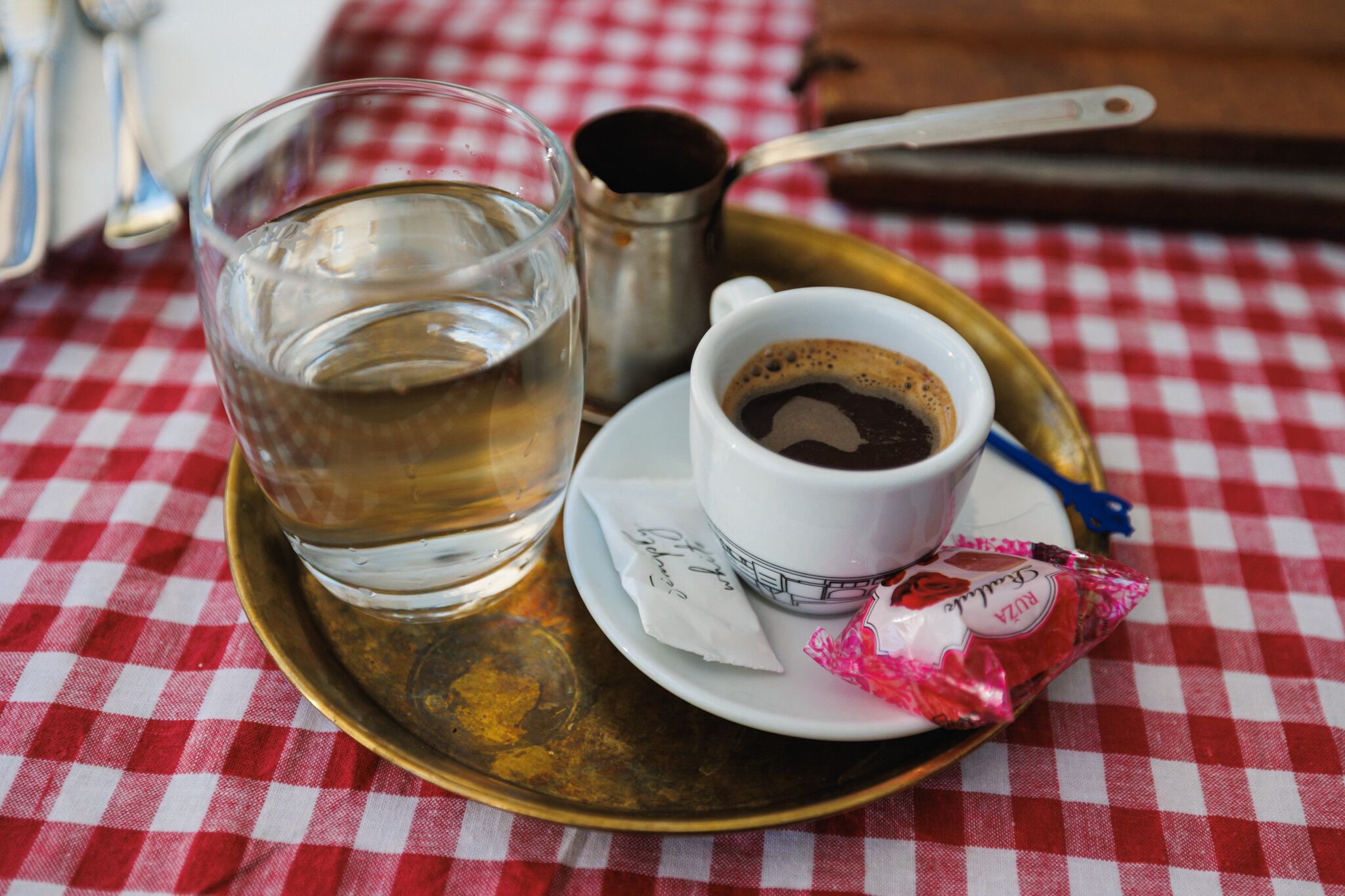 A cup of domaća kafa on a metal tray at Kafana “?” in Belgrade, with a long-handled džezva, water and wrapped ratluk.