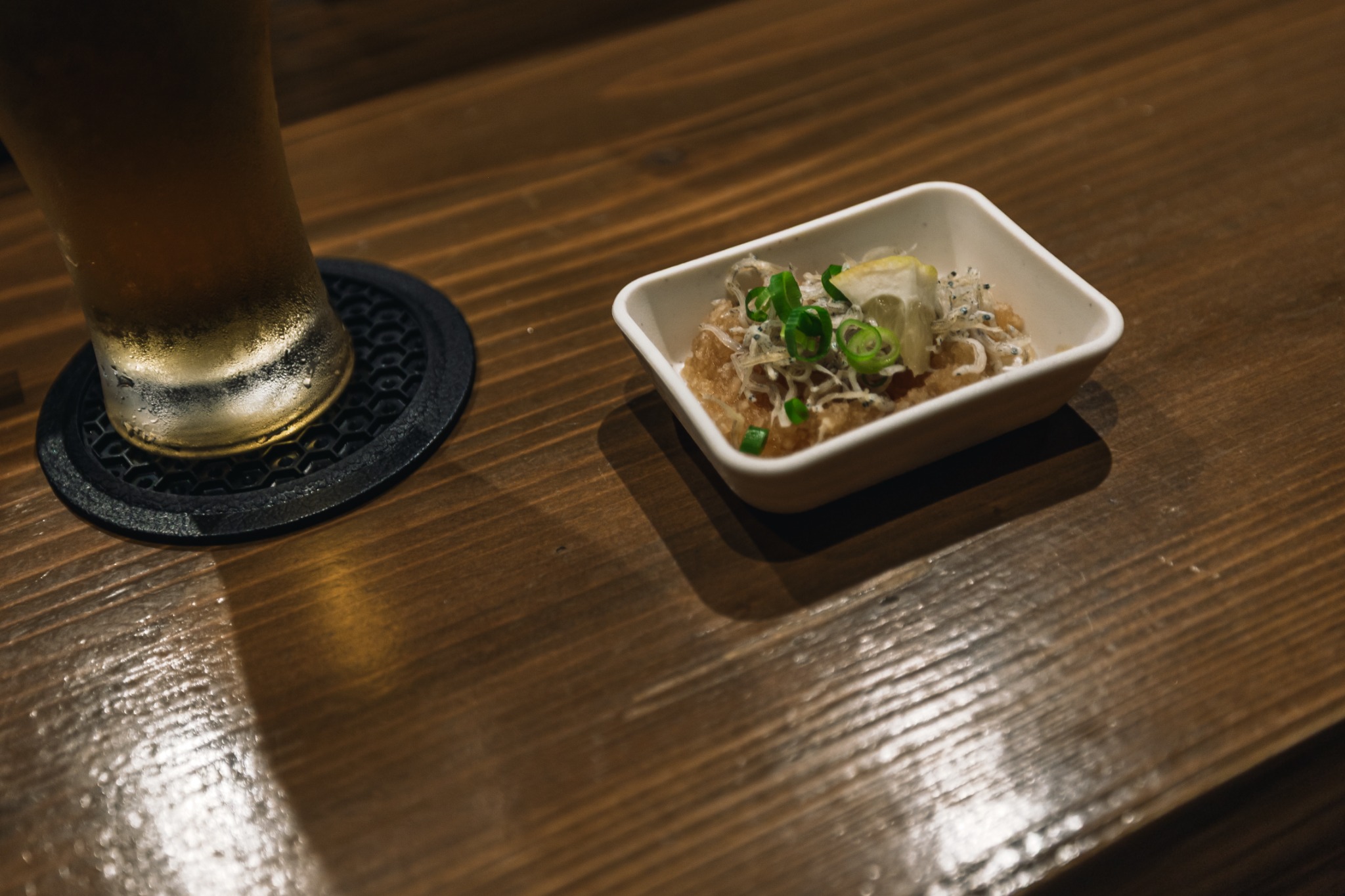 A small appetiser in a white square dish beside a drink on a wooden counter.