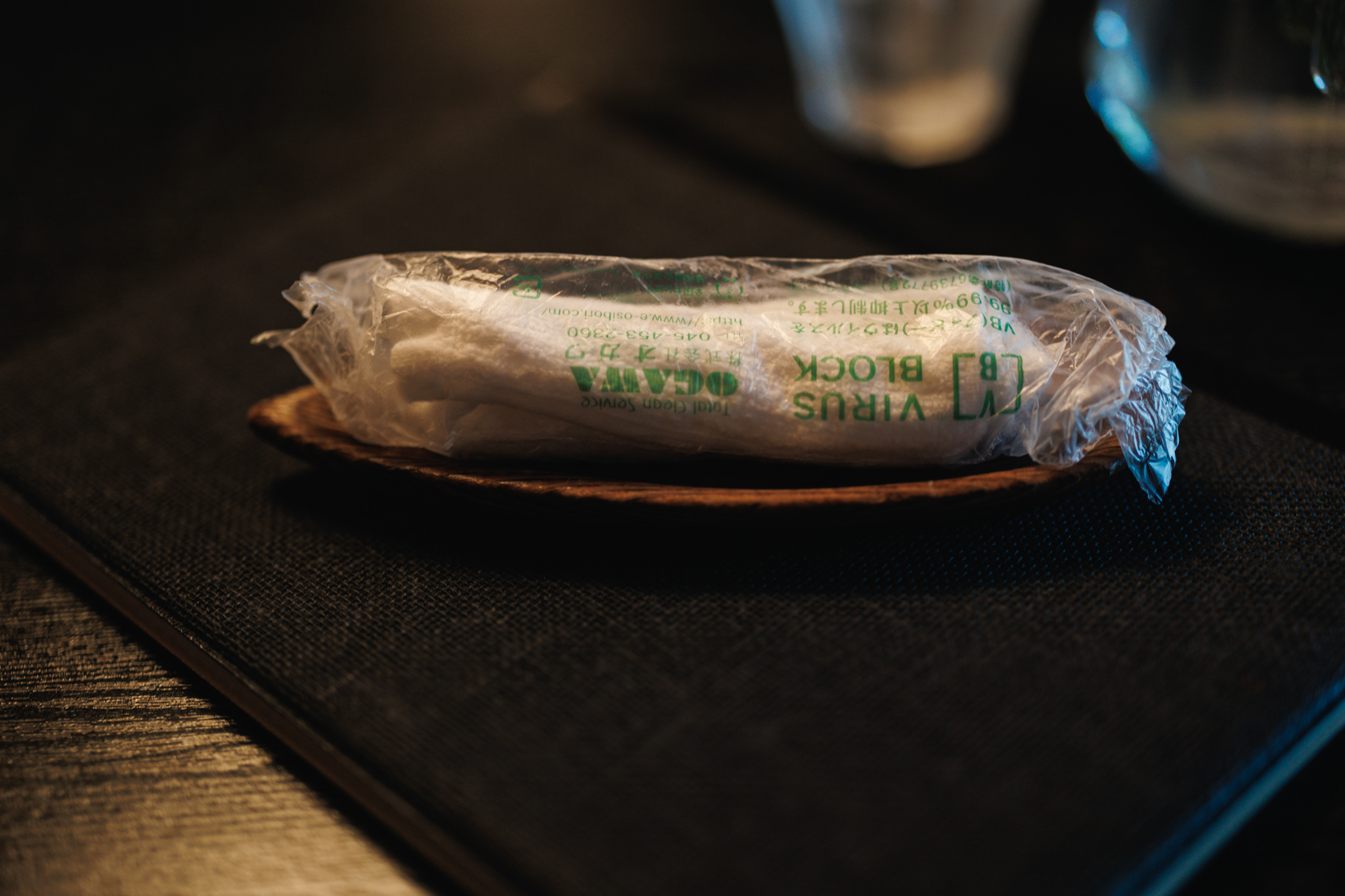 A rolled white hand towel in a clear wrapper rests on a small wooden tray.
