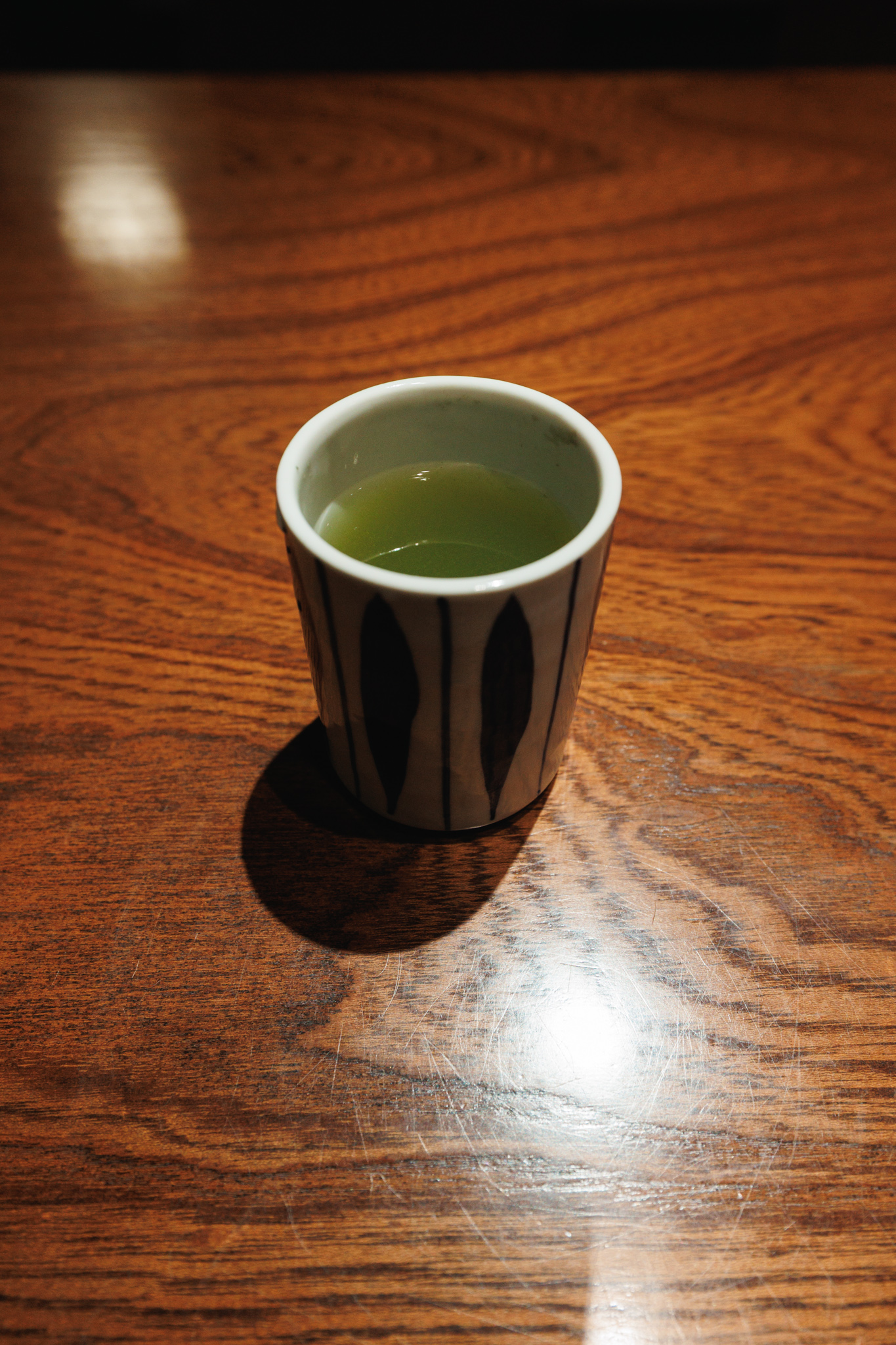Green tea in a patterned ceramic cup on a wooden restaurant counter.