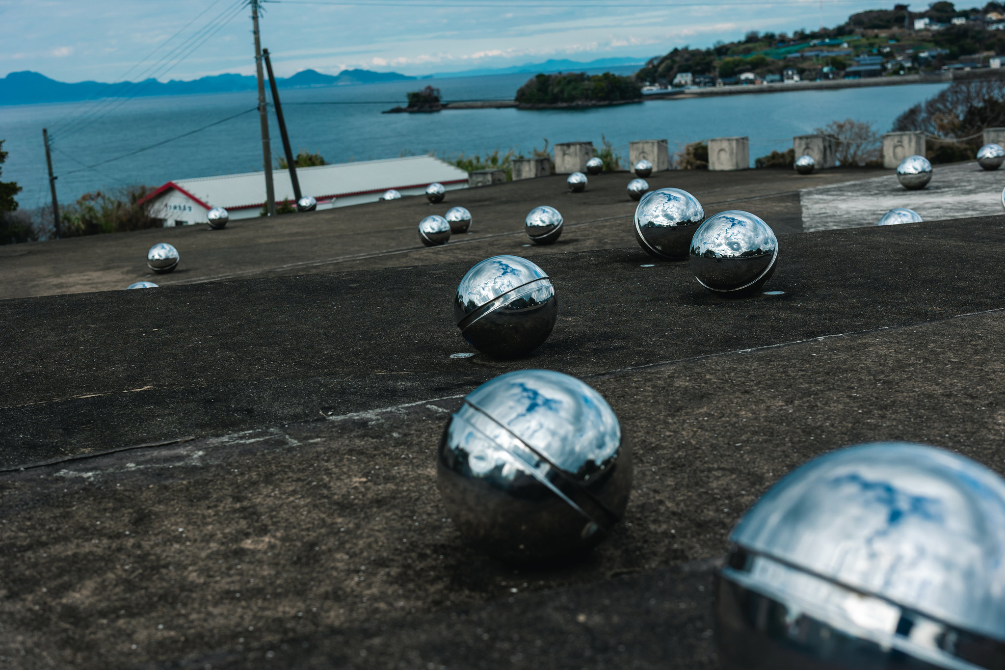 Polished steel spheres on the terraces of the Minamata Memorial, with Minamata Bay and its distant shore behind them.