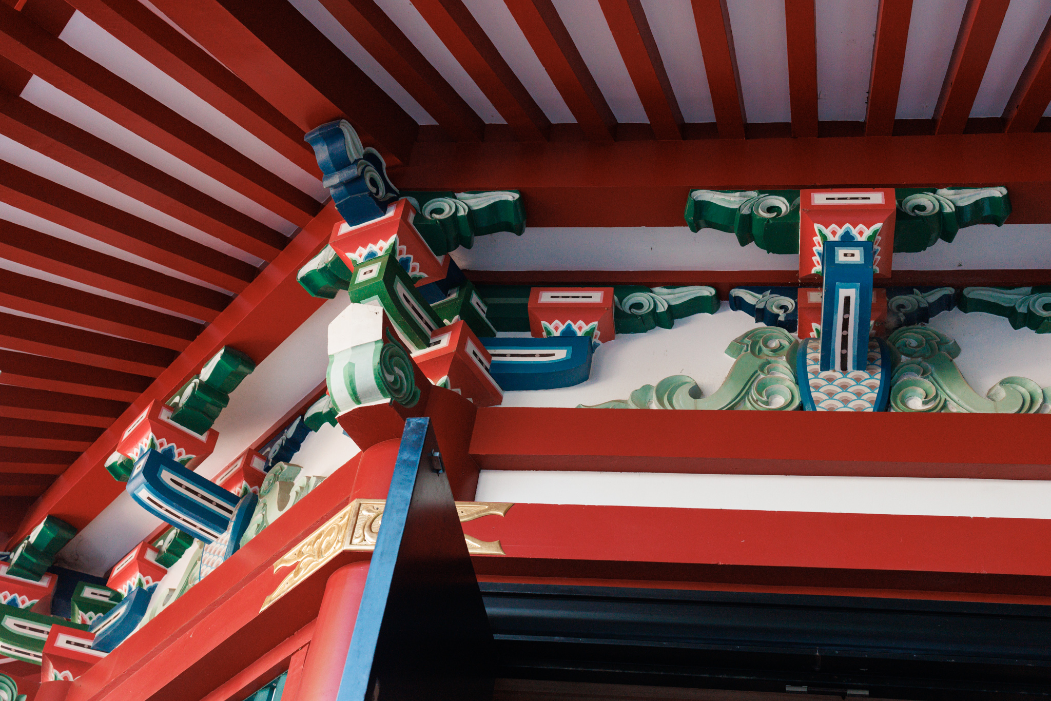 The eaves of a red shrine hall seen from below, with brackets painted in green, blue and white and carved wave shapes