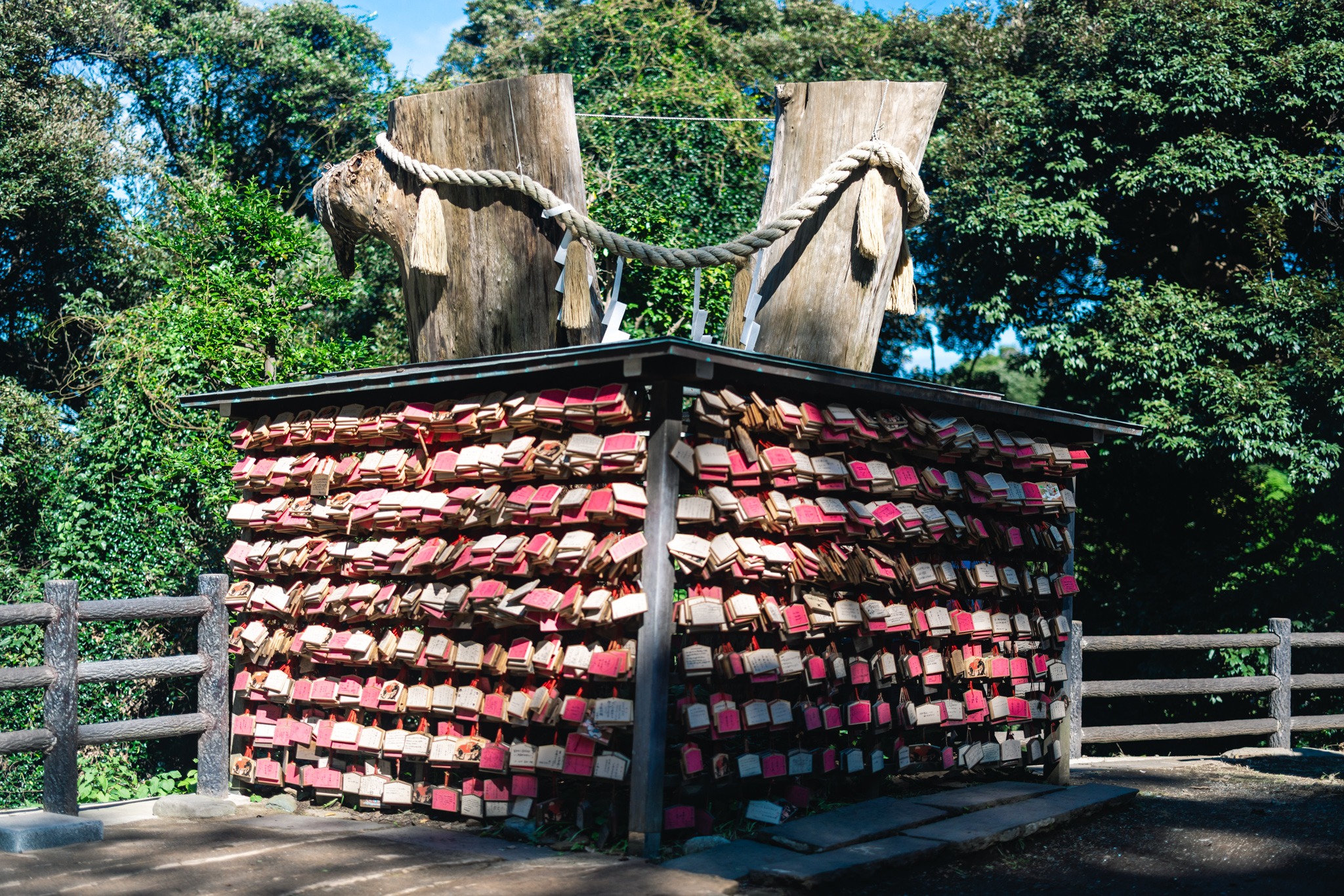 Two cut-off tree trunks joined by a thick sacred rope, standing above a stand covered on every side with rows of pink and wooden prayer plaques