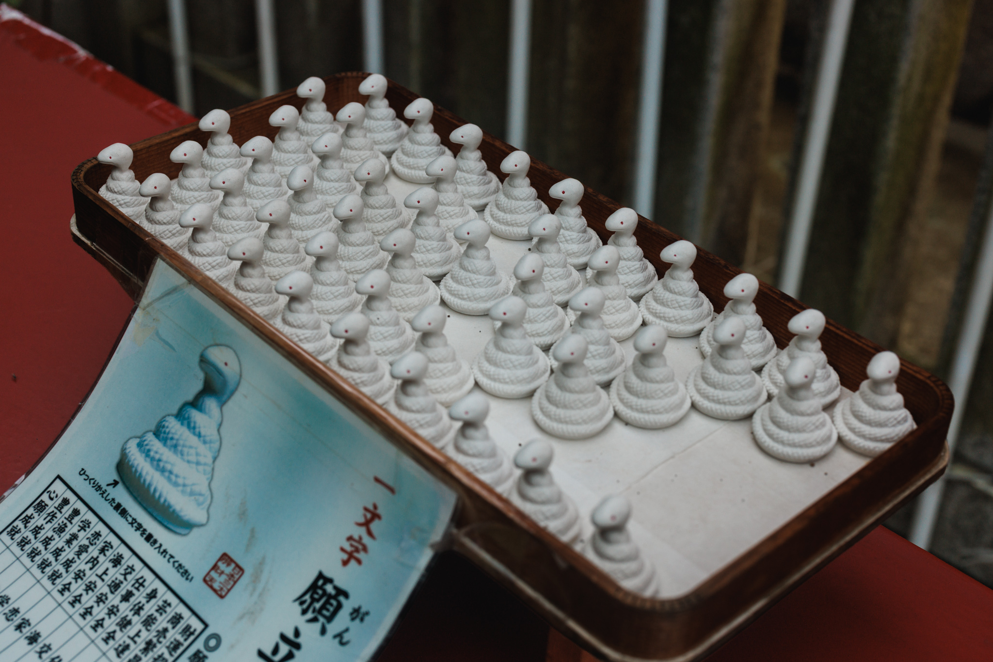 Rows of small white coiled snake figures with red eyes on a wooden tray, beside a printed sign about writing a one-character wish