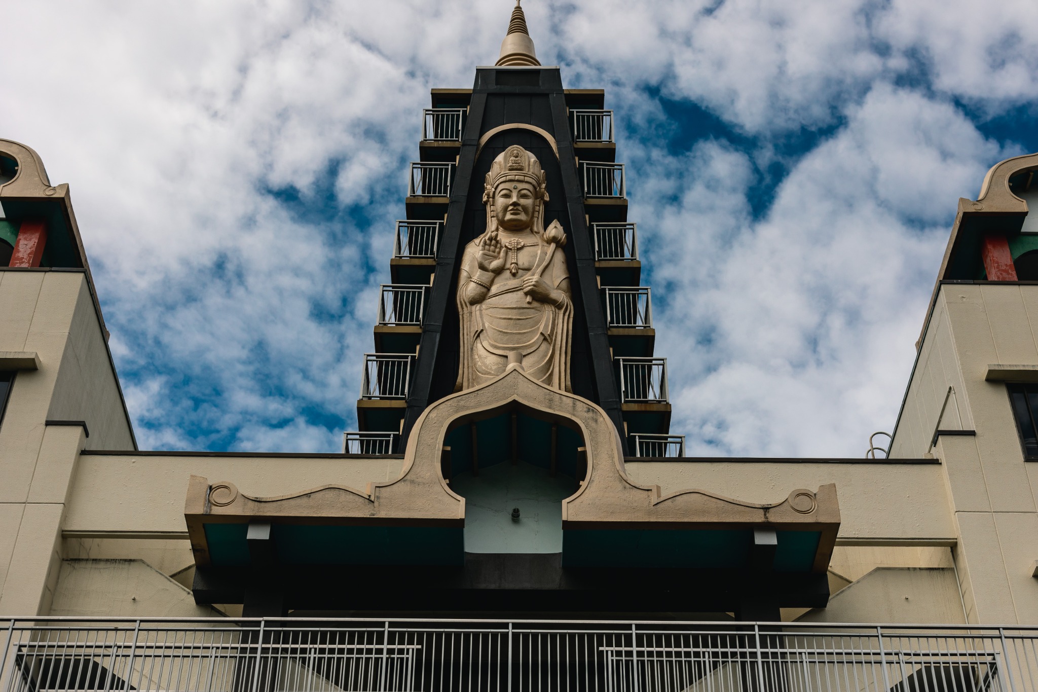 Golden Shō Kannon rising above Entsuji Temple, with rows of balconies on either side of the modern temple building in Tokyo.