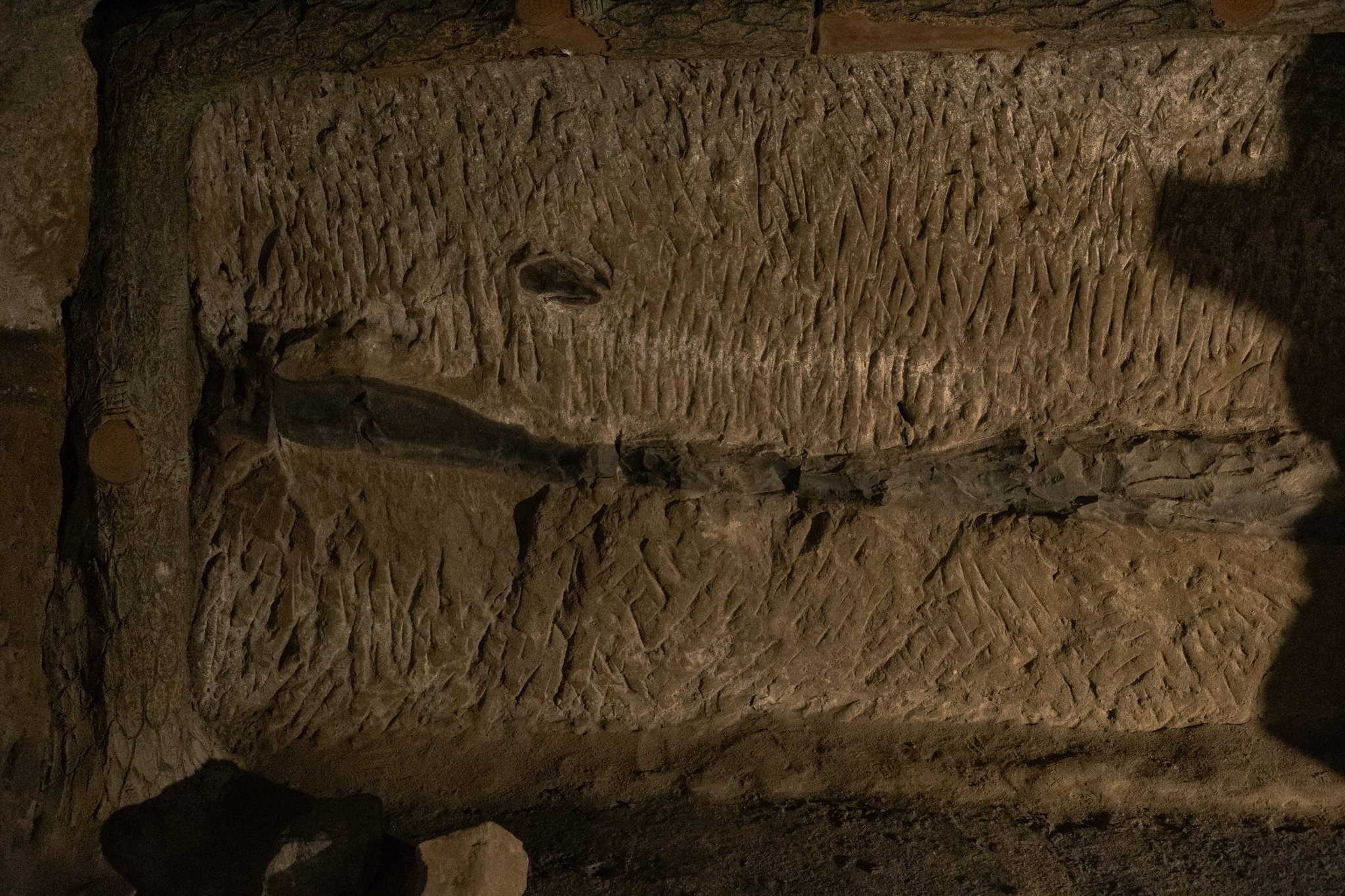 Close view of a rock wall covered with short, narrow tool marks in rows, crossed by a dark seam, lit from the side