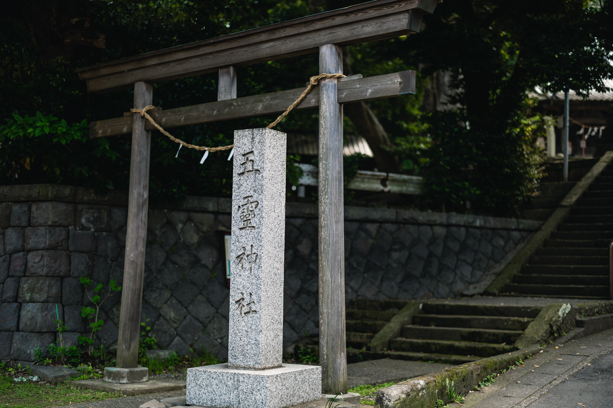 The wooden torii and stone name marker at Goryō Shrine, with the approach climbing into the trees.