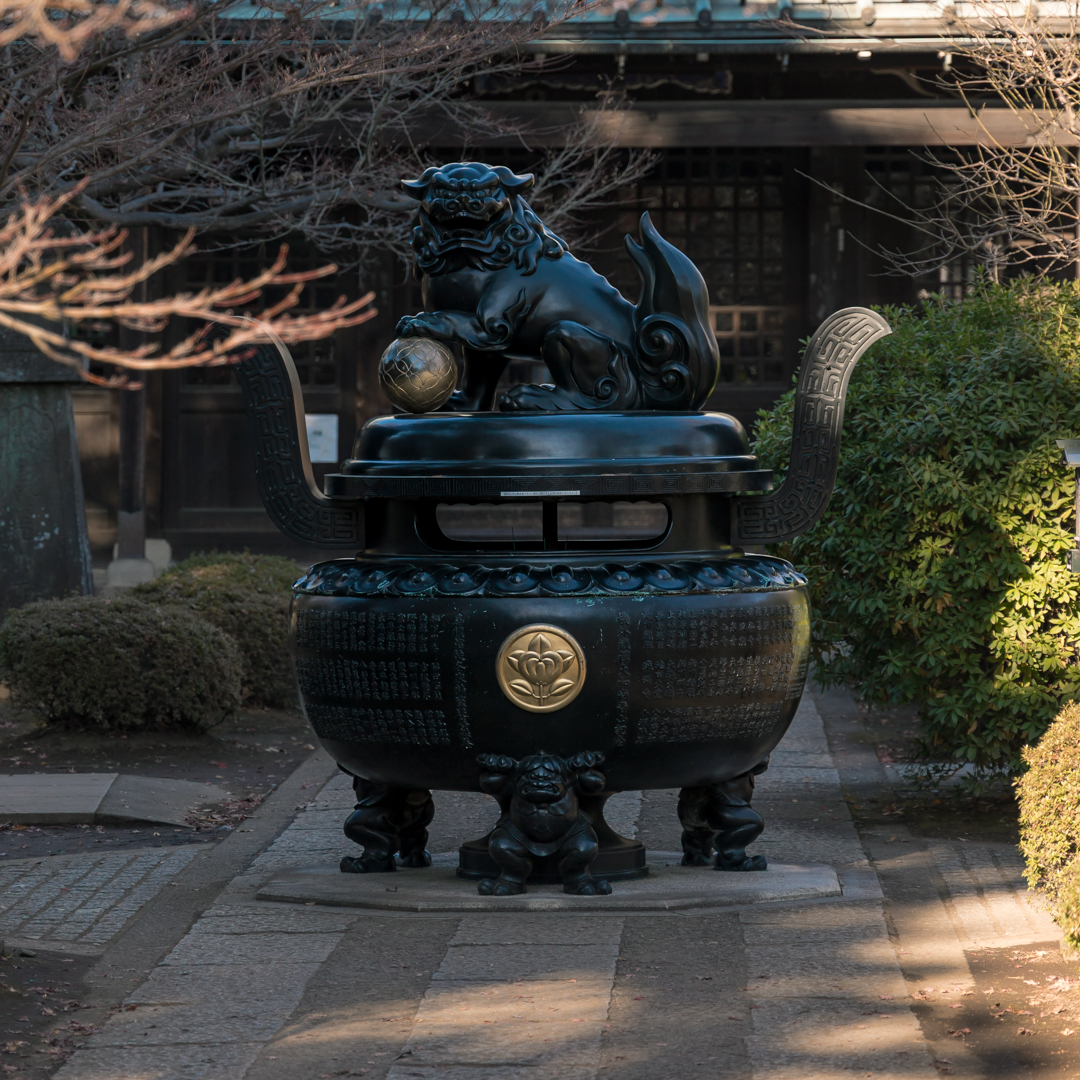 Bronze incense burner at Gotokuji with a shishi on top and small crouching figures supporting it below.