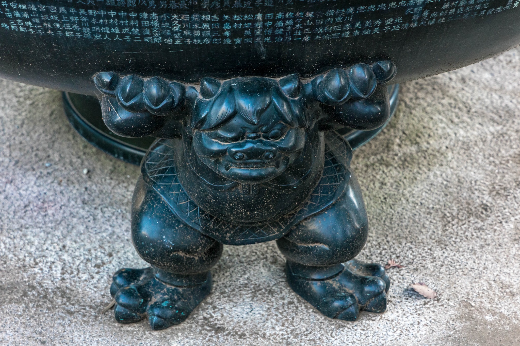 Close-up of one of the crouching figures supporting the large incense burner at Gotokuji Temple.