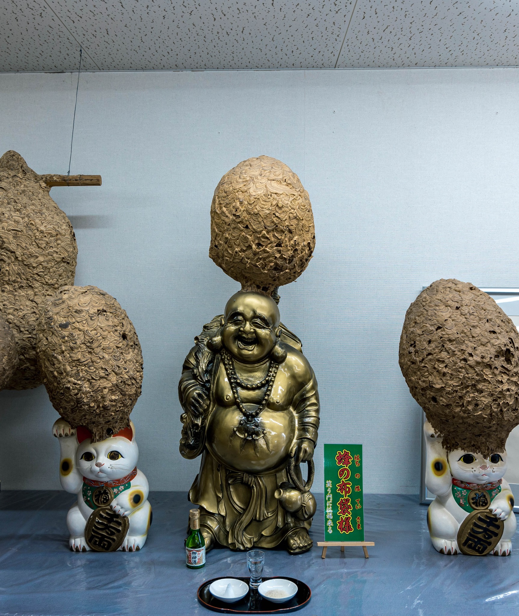 A seated figure flanked by two maneki-neko, surrounded by hornet nests inside Hachi Tengoku in Nagano.