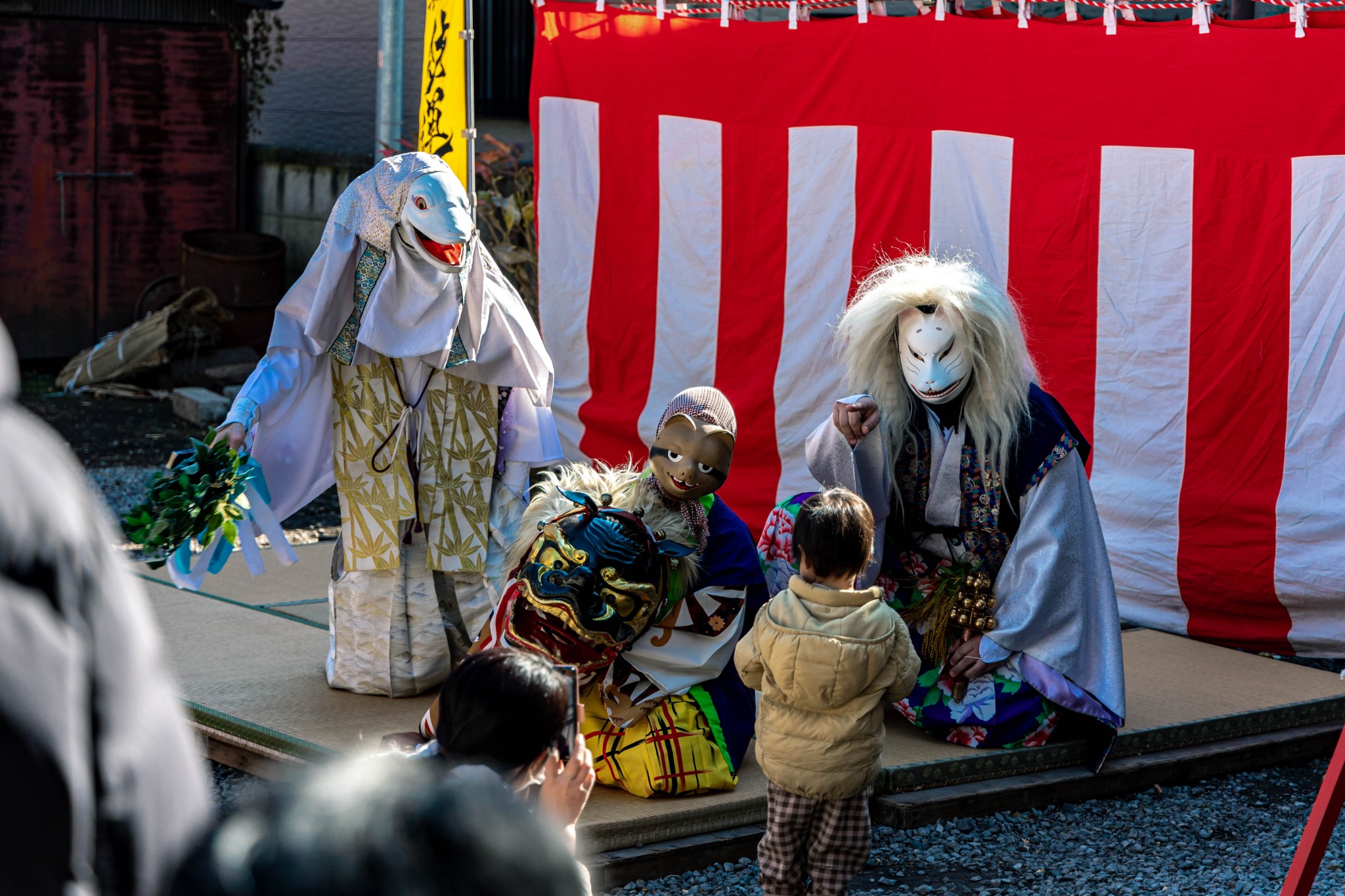 A white snake, masked performers and a lion head facing a small child at Hebikubo Shrine.