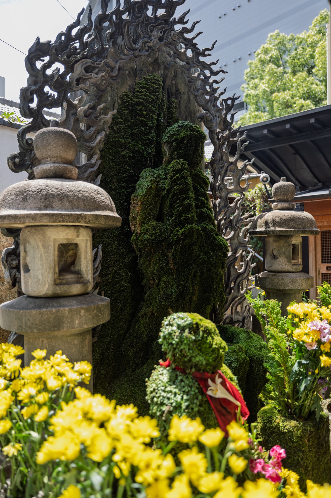 Moss-covered Mizukake Fudō at Hozenji Temple in Osaka, surrounded by stone lanterns and flowers.