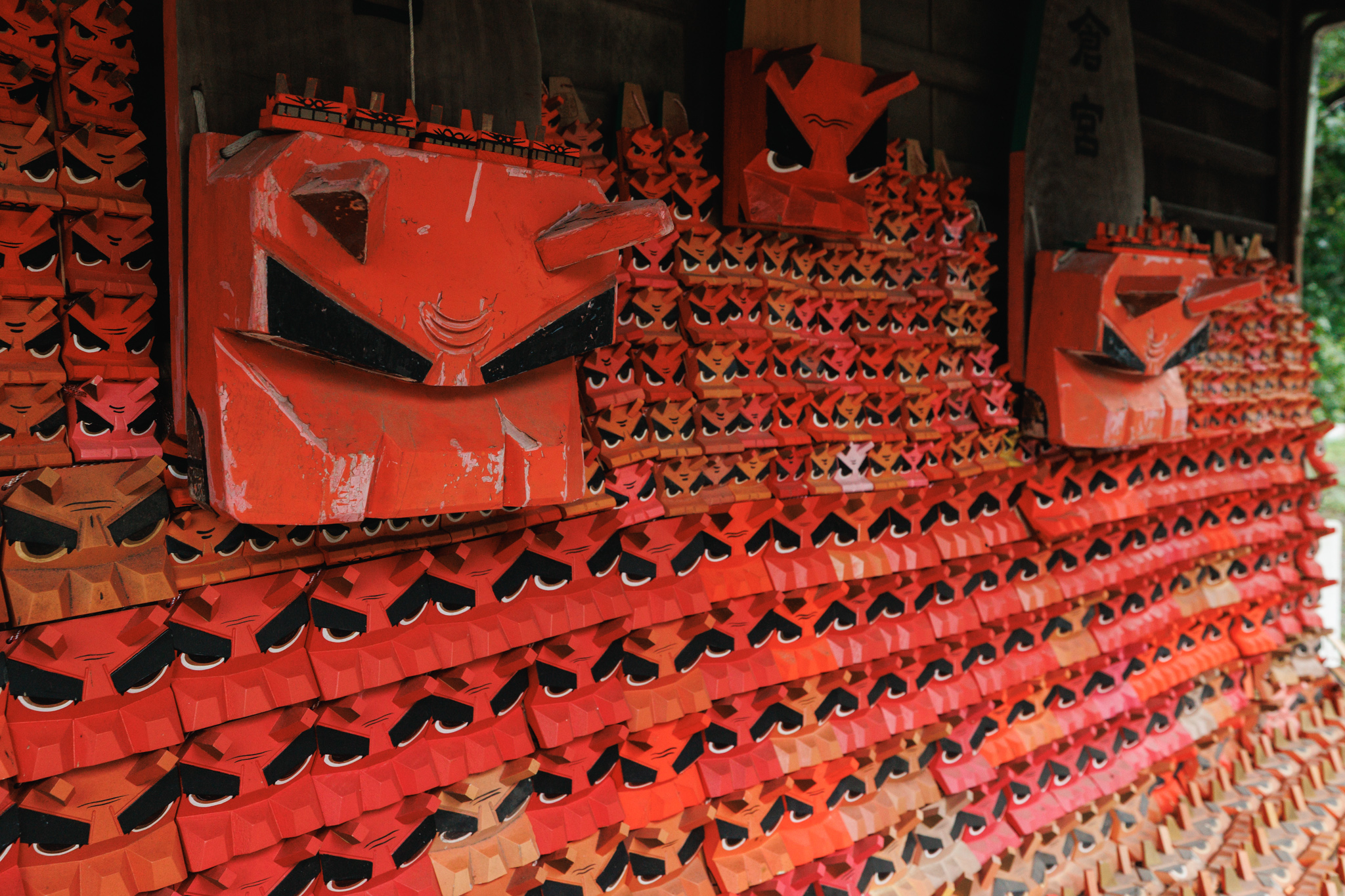 A wall of red wooden lion heads at Kamakura-gū, two large ones rising above hundreds of small ones