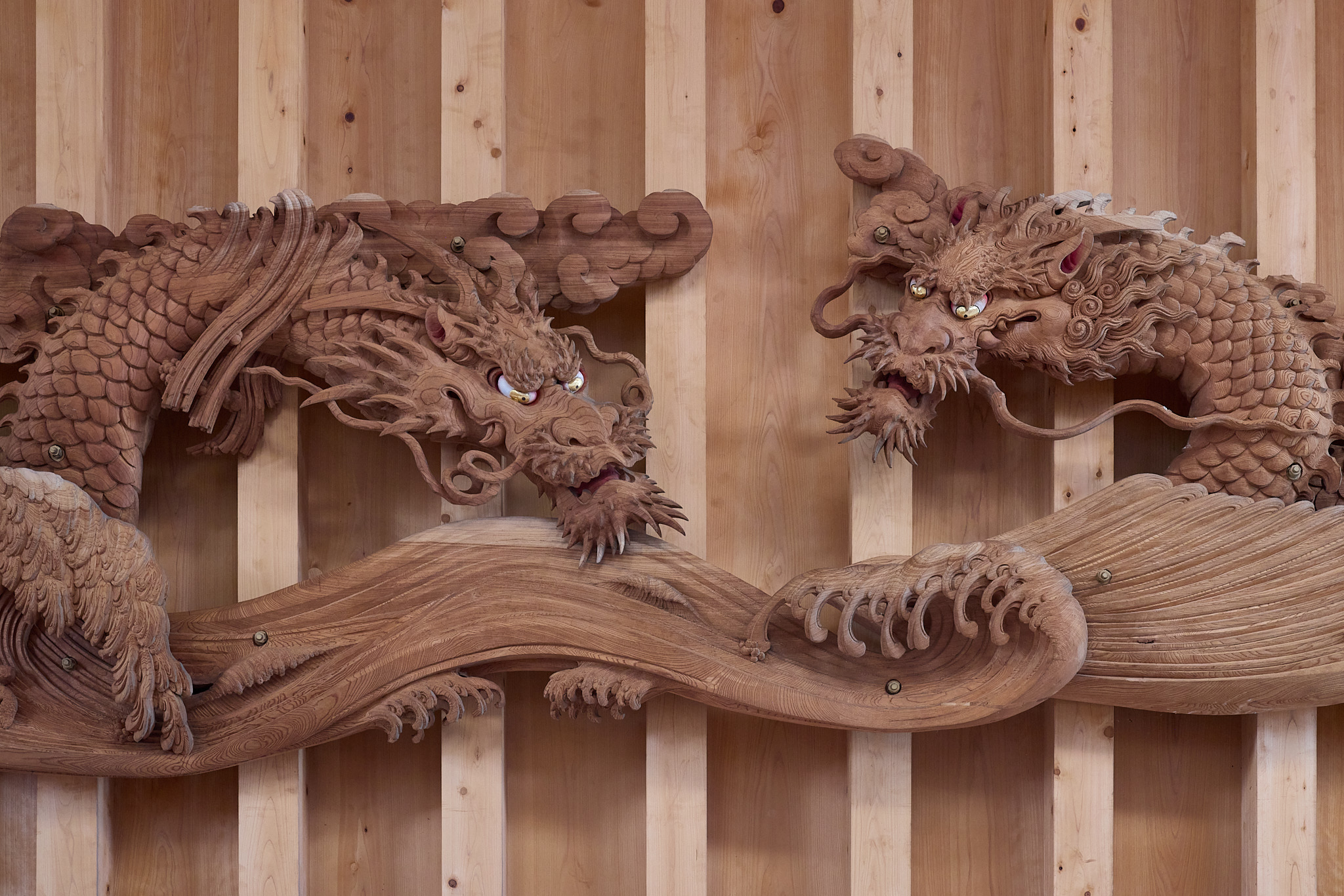 Two carved wooden dragon heads facing each other, with gold eyes, long whiskers, red around the mouths and scaled bodies, against vertical wooden boards