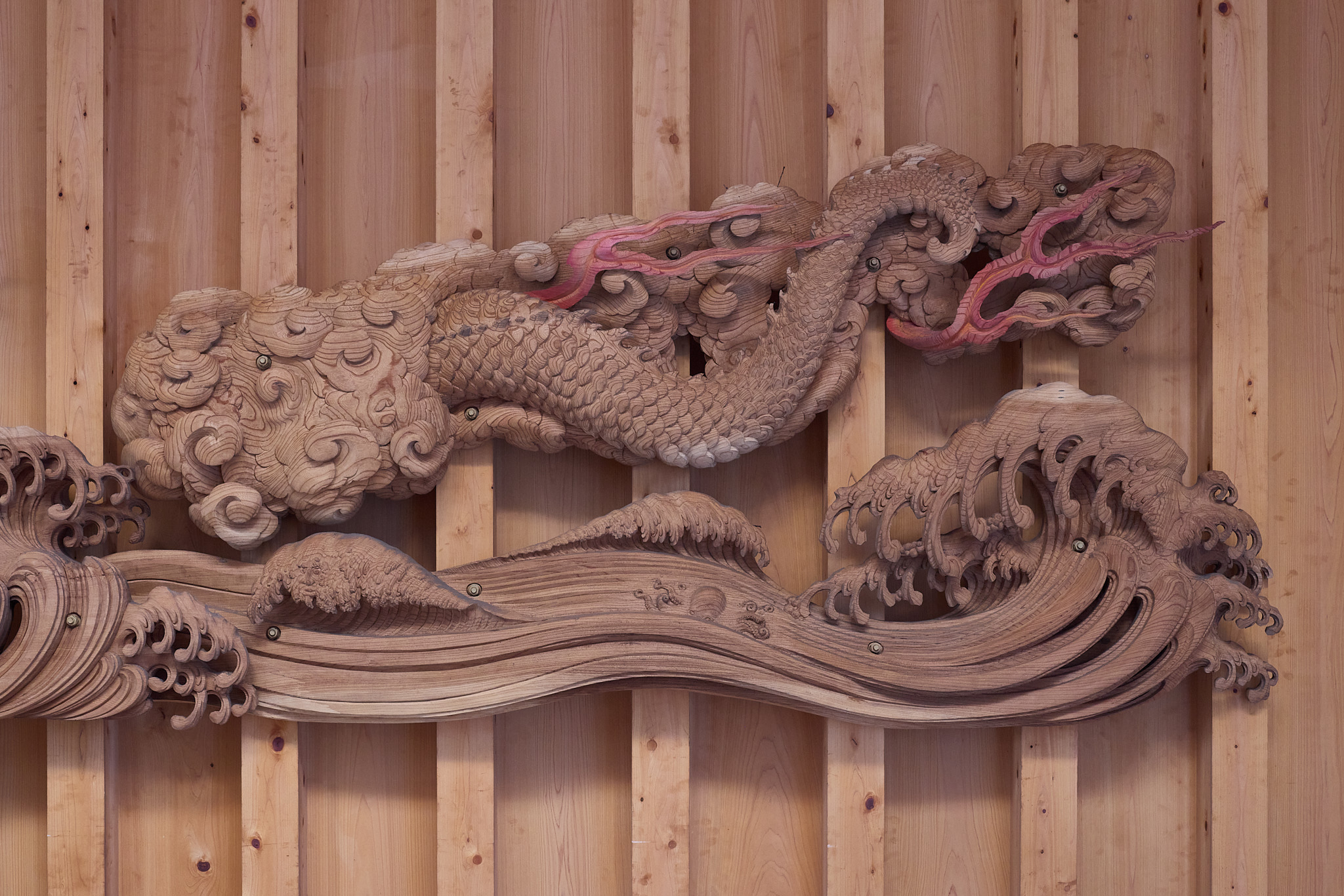 A curving scaled section of the carved dragon above a broad wooden wave, with a small carved octopus in the wave below