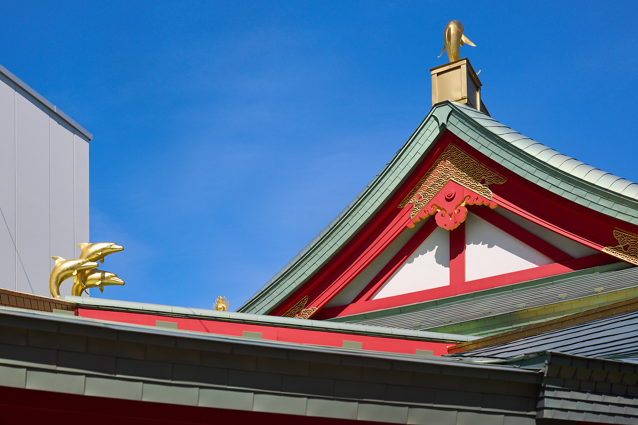 Gold dolphin figures on green roofs with red and gold trim against a blue sky, three together at lower left and one on its own at upper right