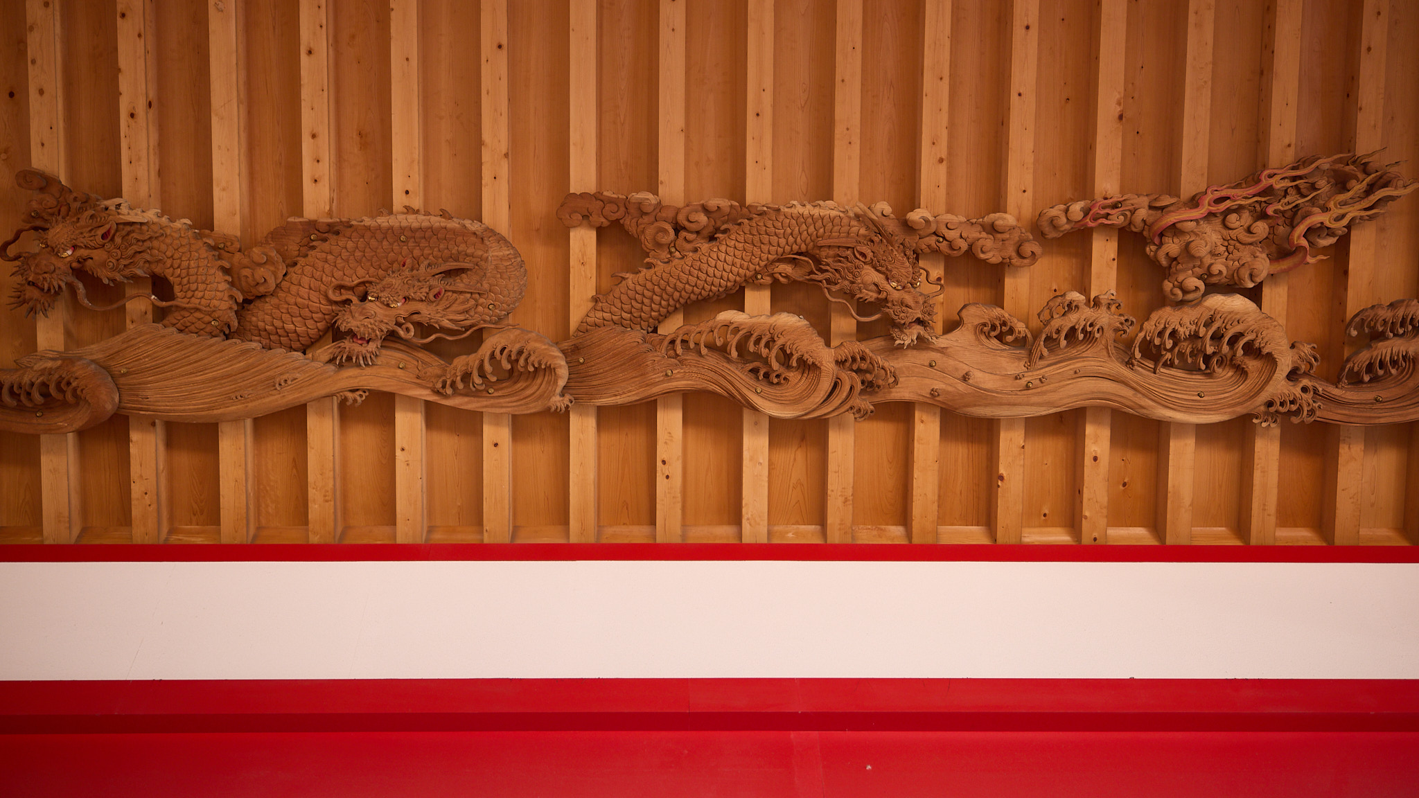 Two carved wooden dragons among clouds and breaking waves on the ceiling, with red-painted flames at upper right, above a red and white beam