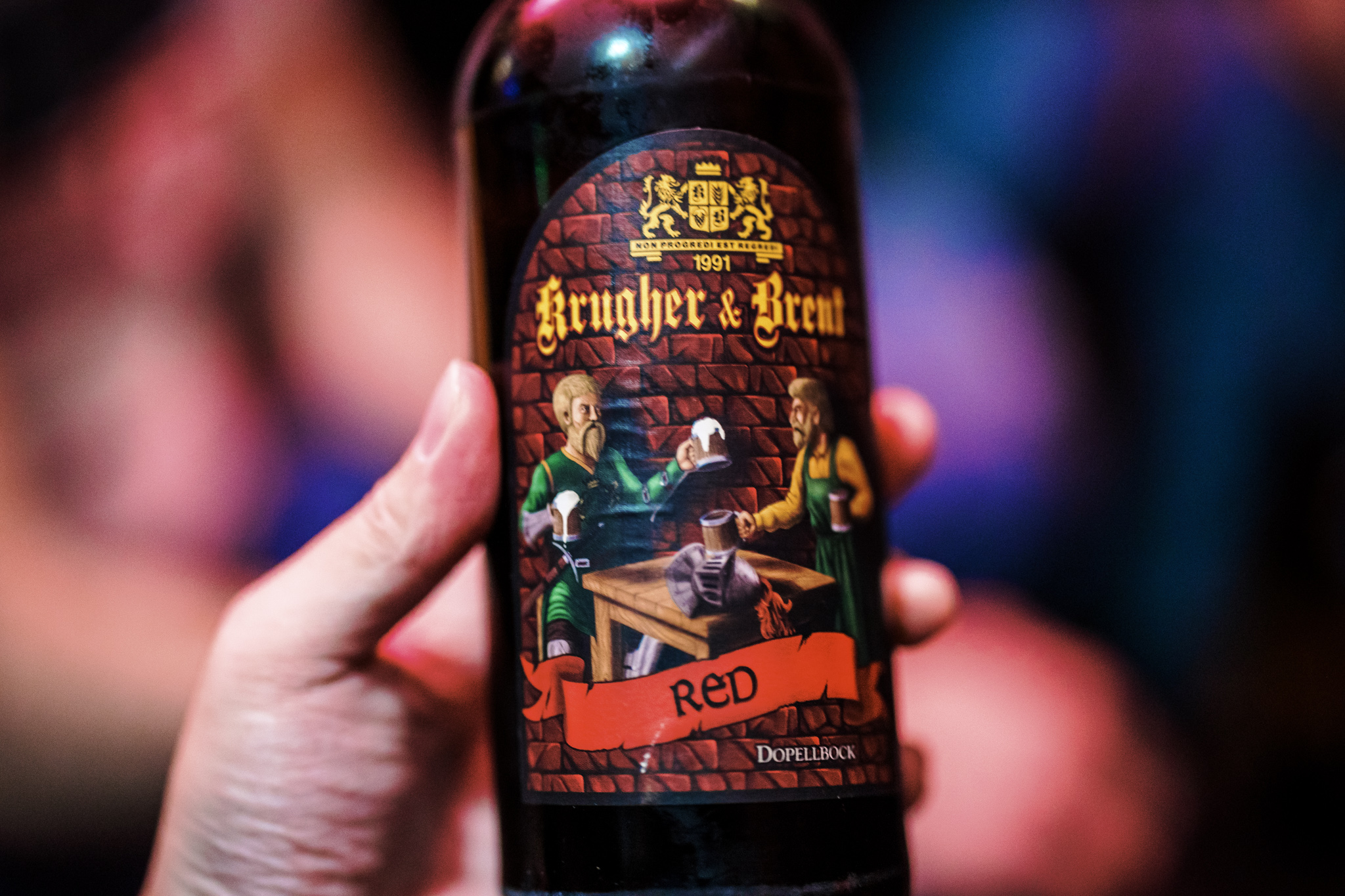 A hand holding a bottle of Krugher & Brent RED doppelbock under red and blue lighting at KOTA 84 in Novi Sad.