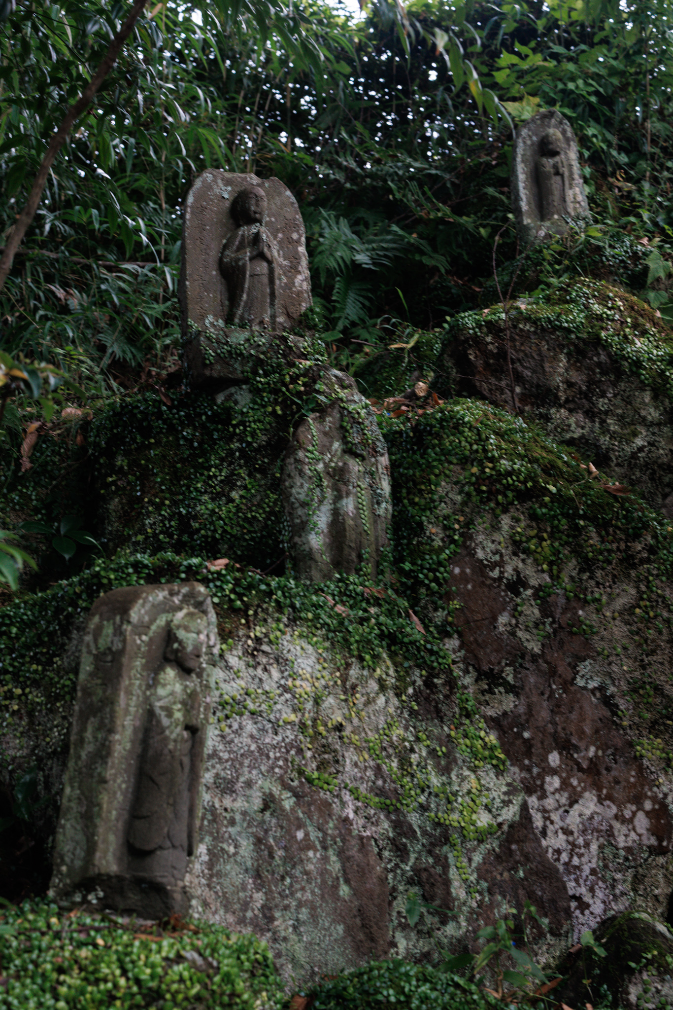 Small carved stone figures set at different heights among mossy rocks and ferns