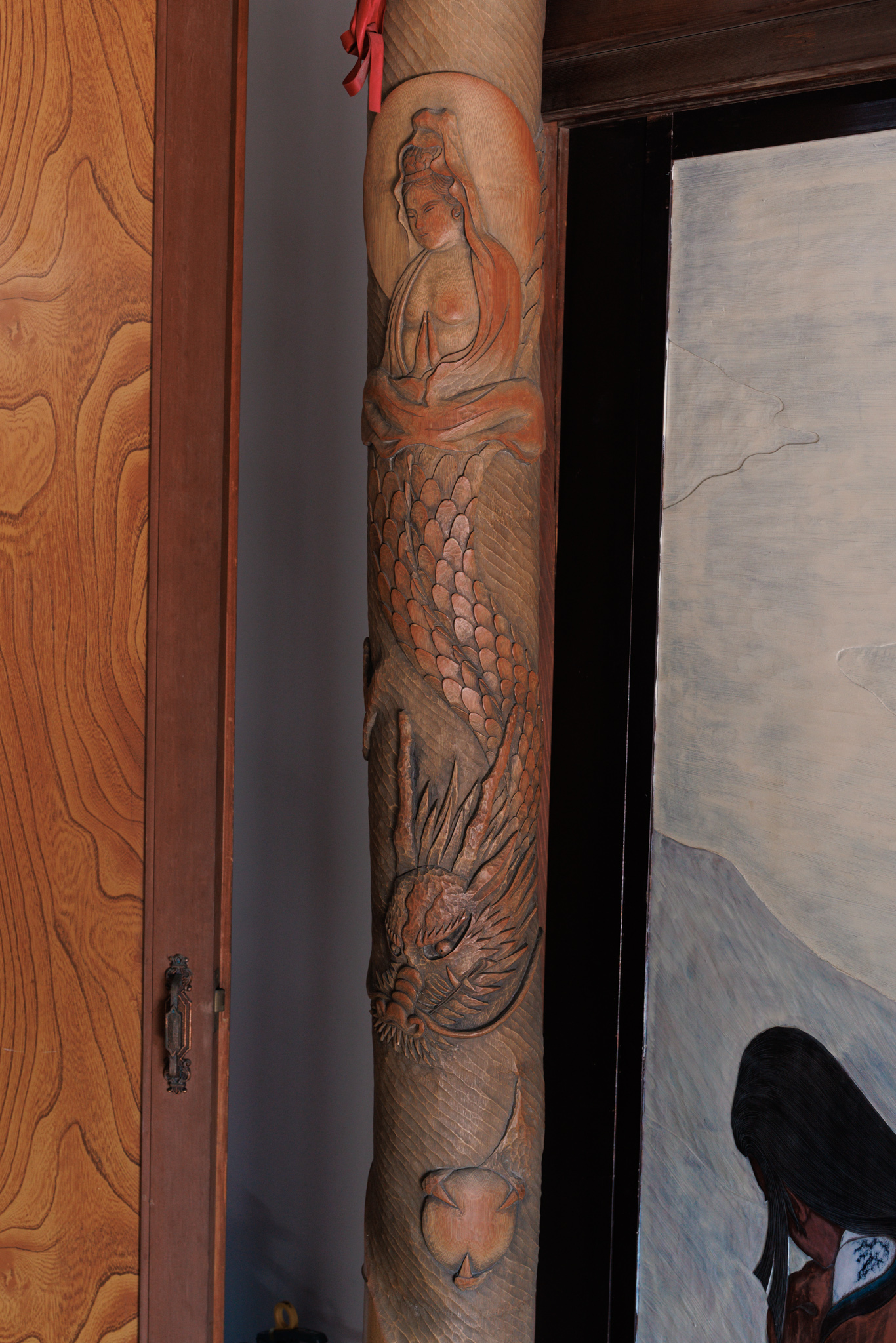 A carved wooden pillar with a seated figure near the top and a scaly dragon coiling down below