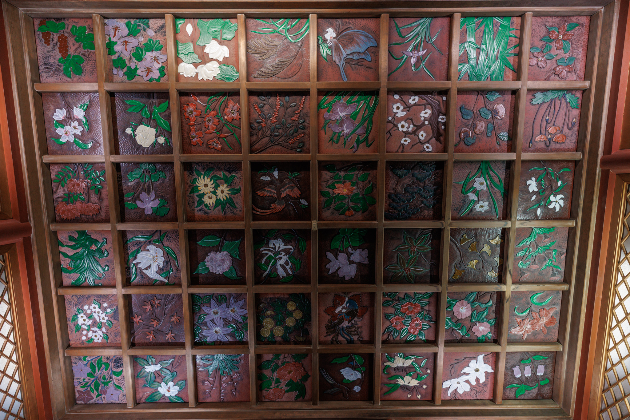 A coffered ceiling of dark wooden squares, each carved and painted with a different flower or plant