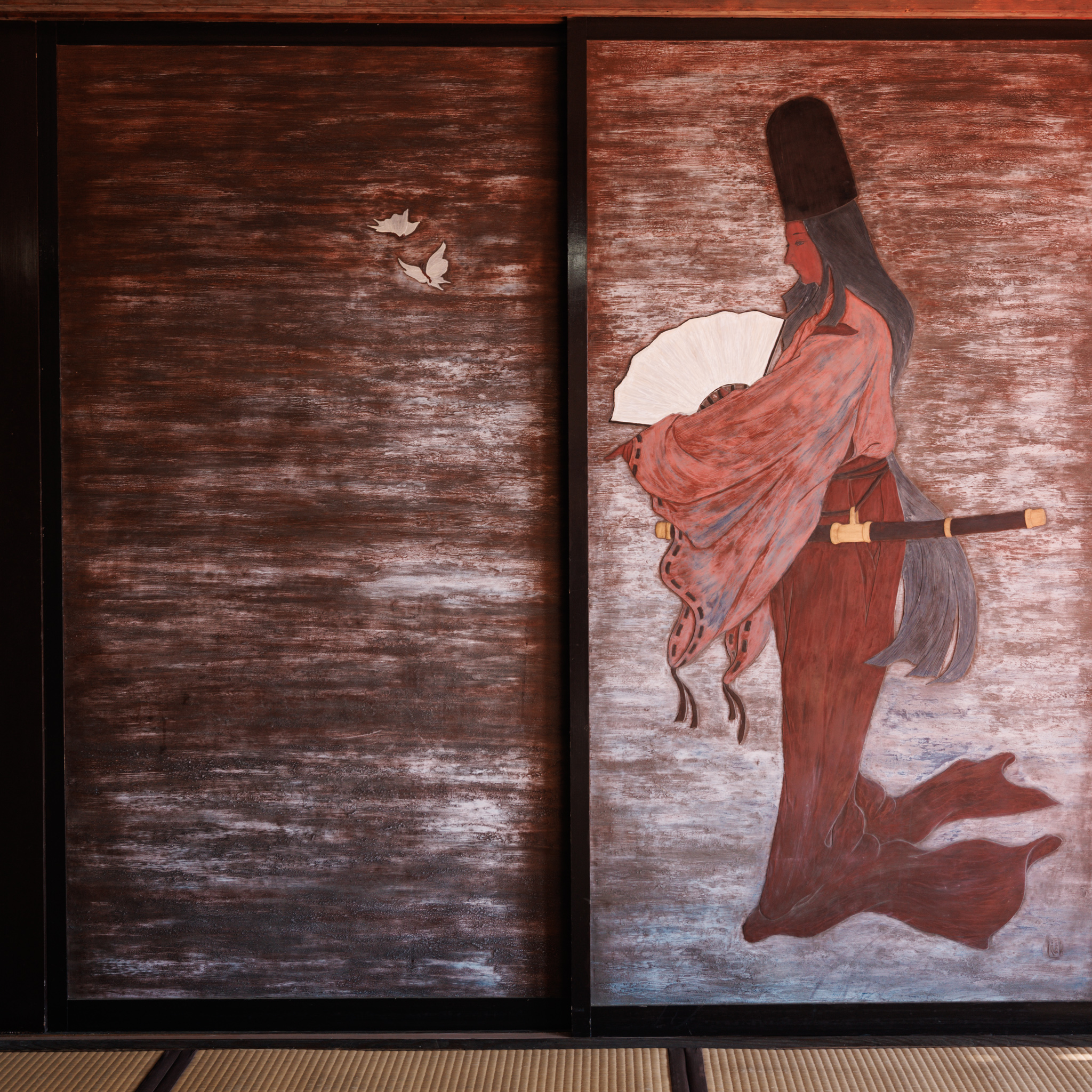 Two sliding doors on a dark red ground, one painted with small white butterfly-like shapes, the other with a figure in a tall black hat and red robes holding an open white fan, a sword at the waist