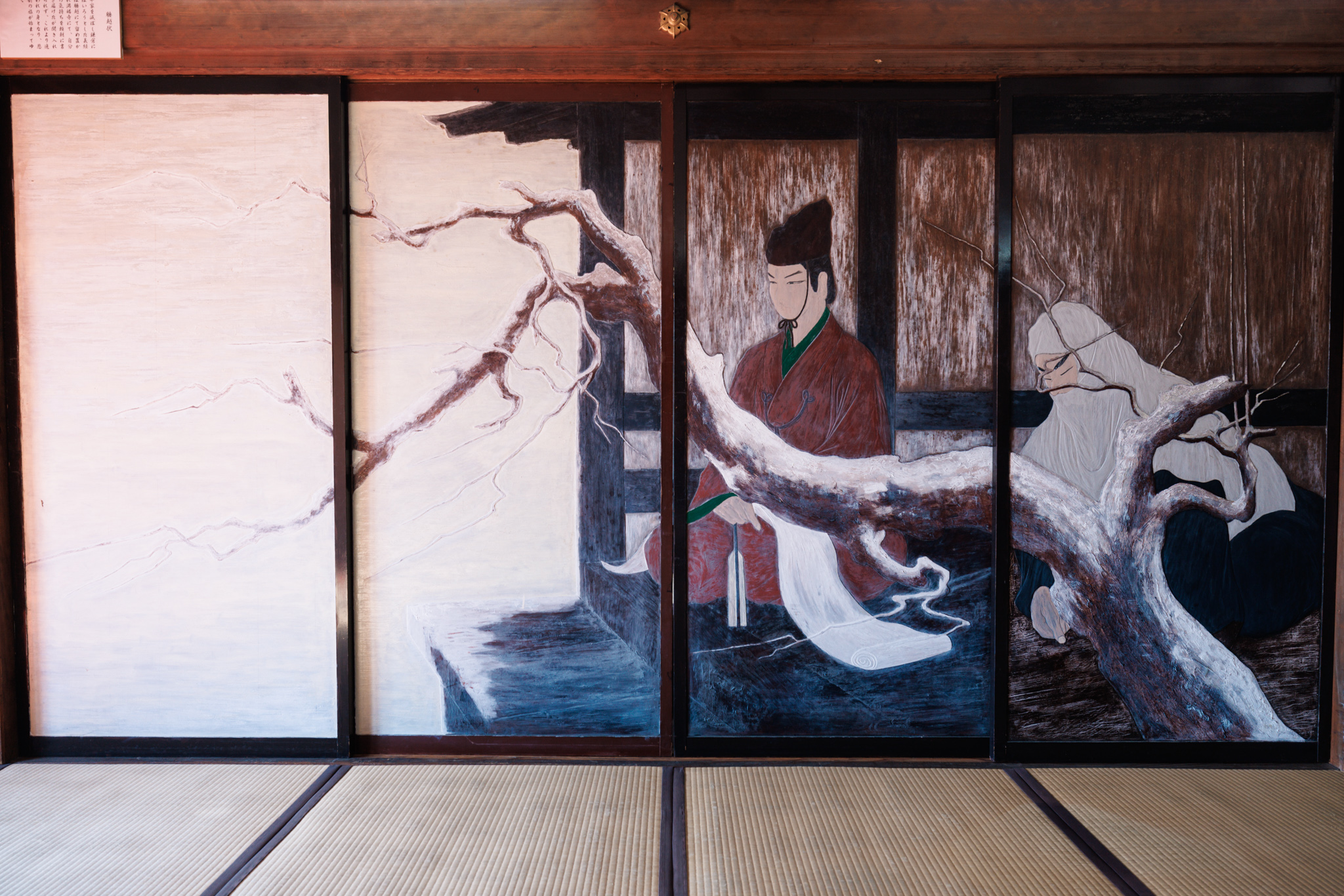 Four lacquered sliding doors painted with a nobleman in red holding a long white scroll and a white-hooded figure behind a pale, gnarled tree trunk, with a label above the doors