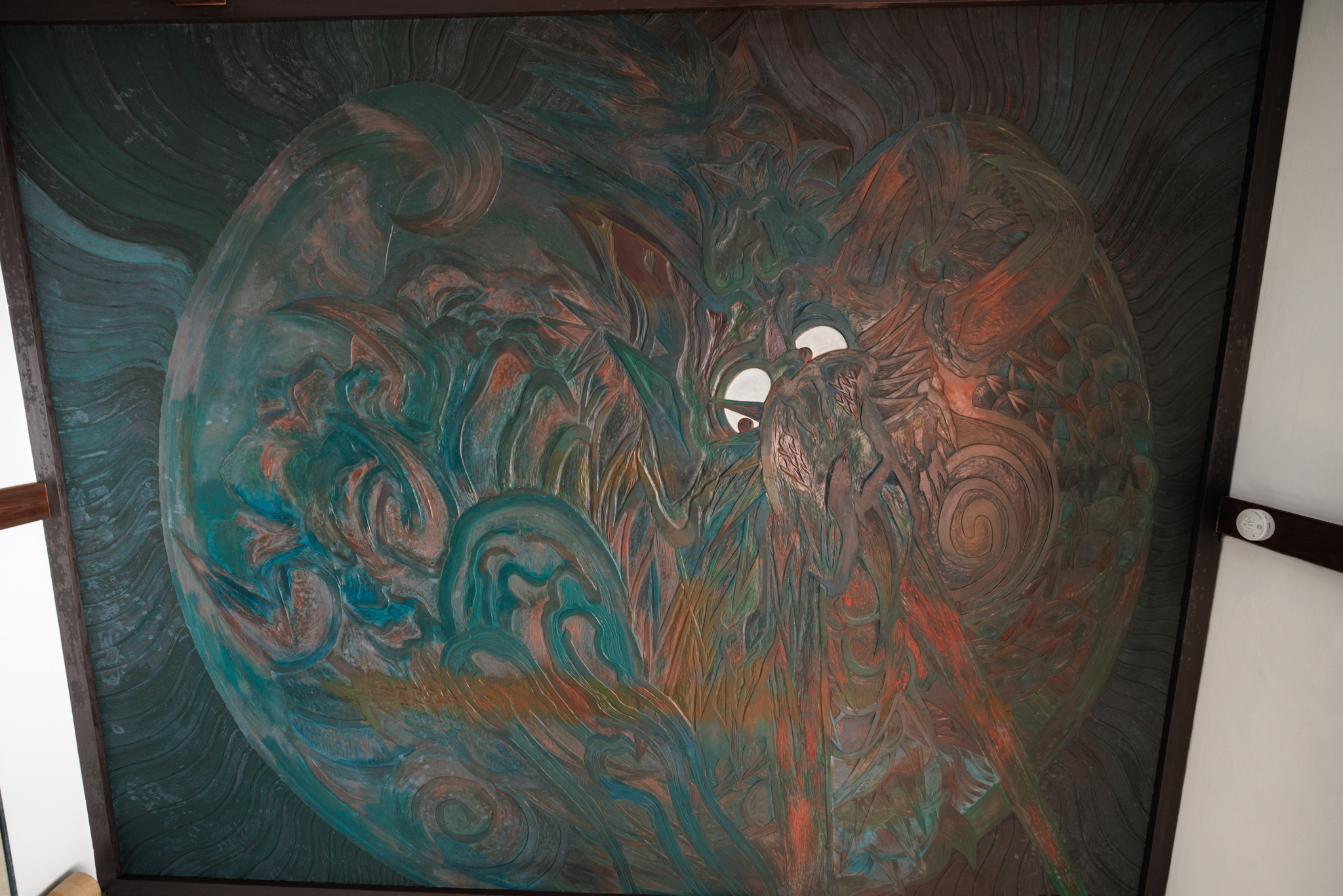 A large circular painting of a dragon’s face with white eyes, in swirling greens and reds