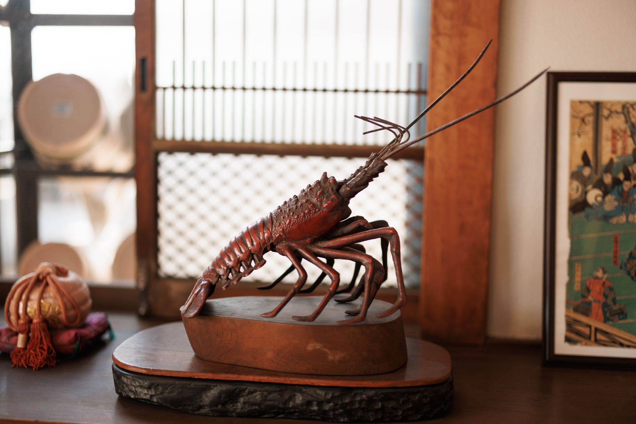 A model of a spiny lobster with long antennae and jointed legs, mounted on a wooden base by a lattice window
