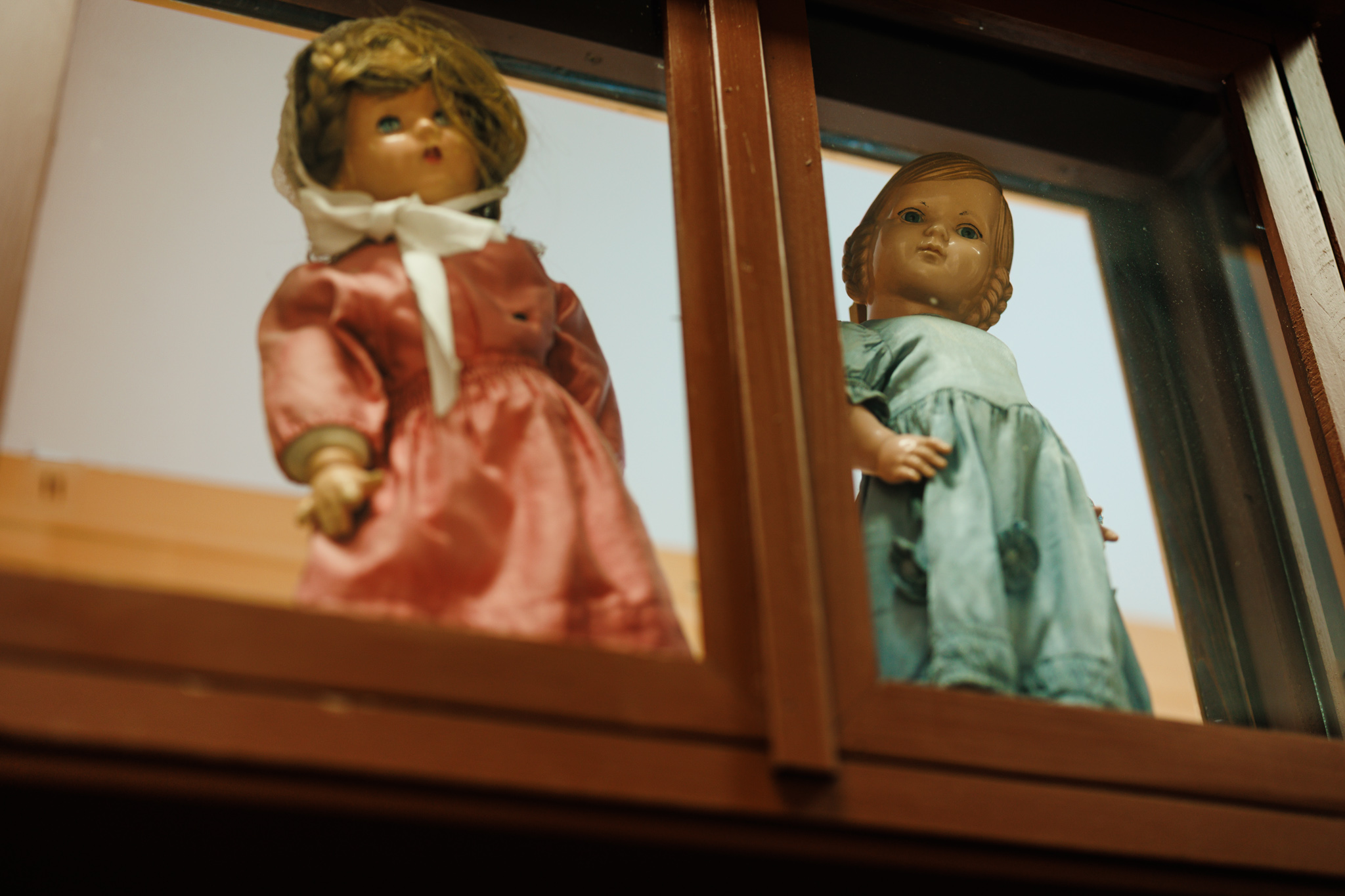 Dolls in pink and pale blue dresses behind a wooden-framed shop window at the Museum of Vojvodina.