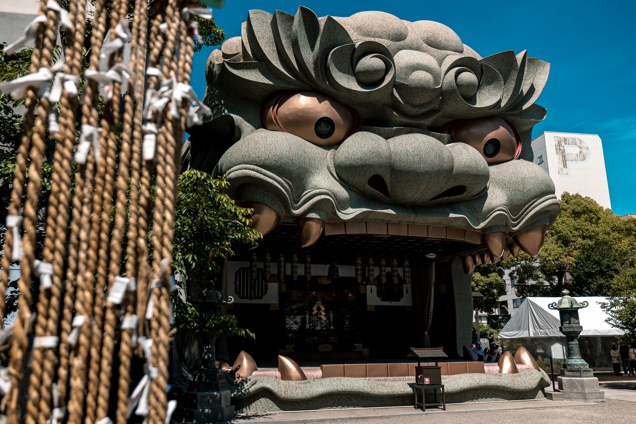 Giant lion-head Shishi-den at Namba Yasaka Shrine in Osaka, with its open mouth forming a stage above visitors in the courtyard.
