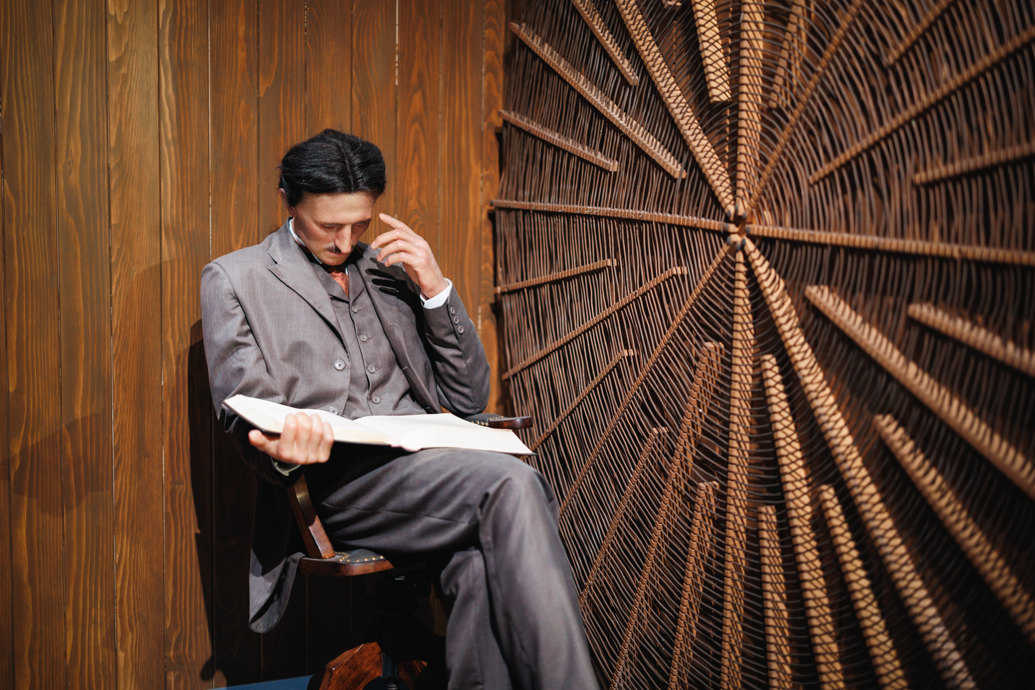 A seated representation of Nikola Tesla reading a book beside a large radial coil at the museum in Belgrade.