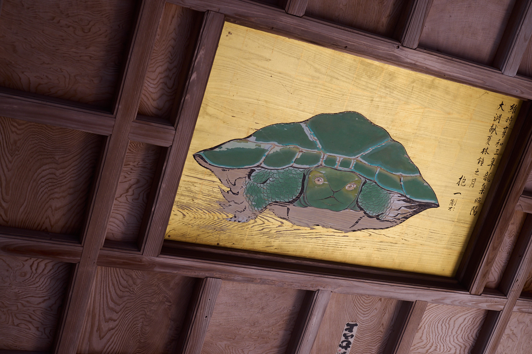 The turtle painting on the shrine ceiling seen from one side, its frame and the surrounding wooden beams running at a slant