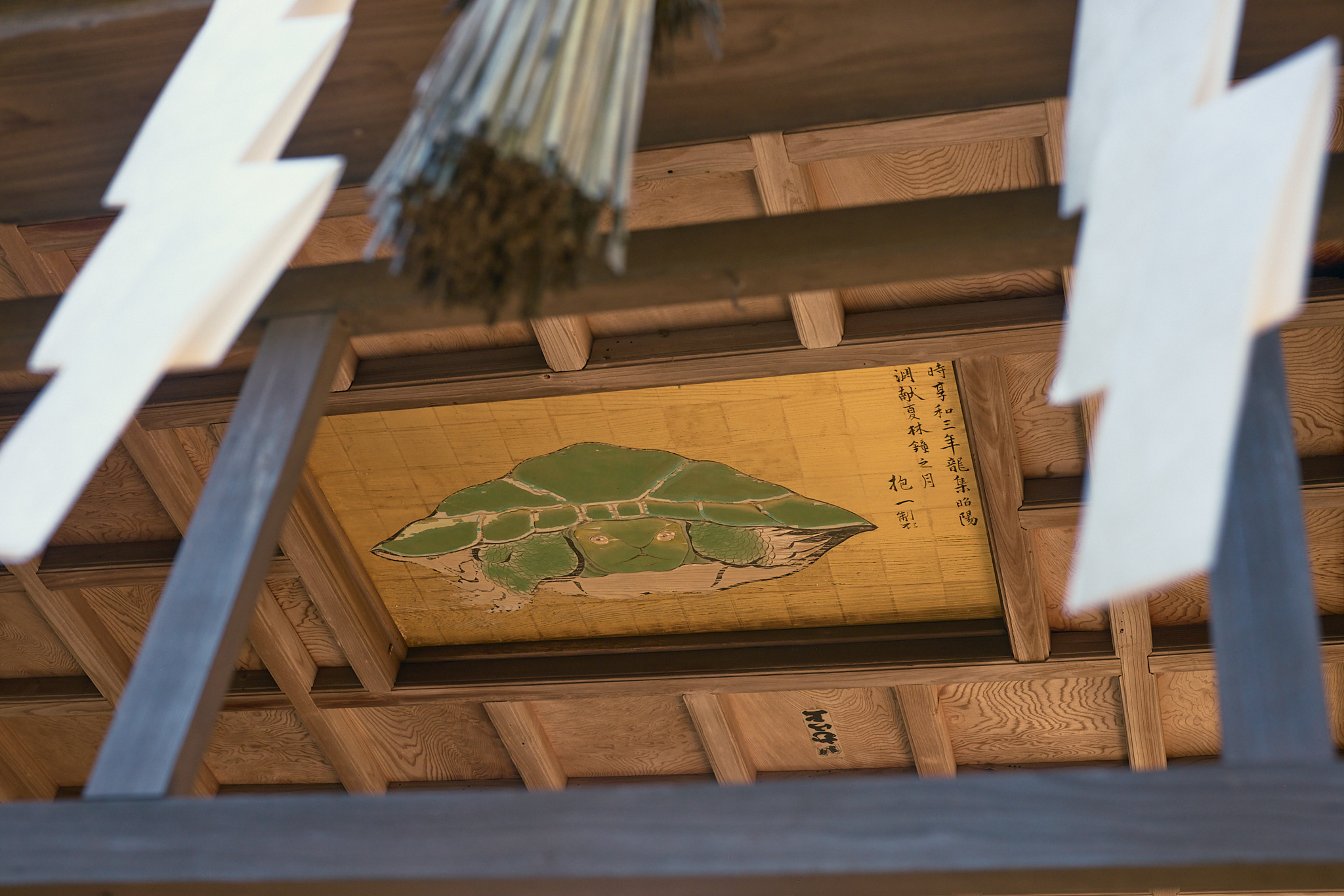 The turtle painting seen from farther back, between white zigzag paper streamers and a straw tassel hanging in the foreground