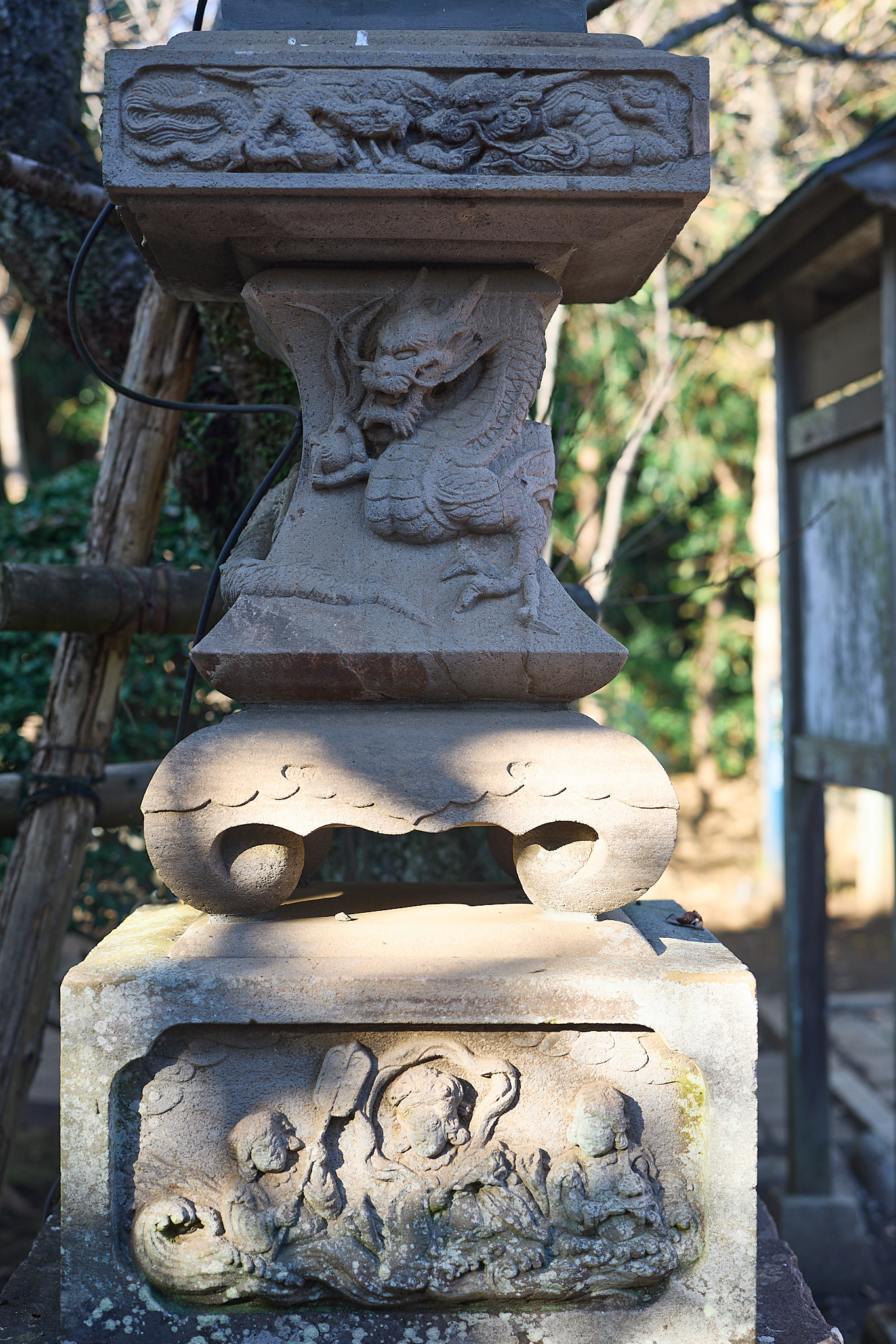 A carved stone lantern pedestal with a dragon along the upper band, another coiling on the shaft, and a relief of a woman and attendants on waves at the base