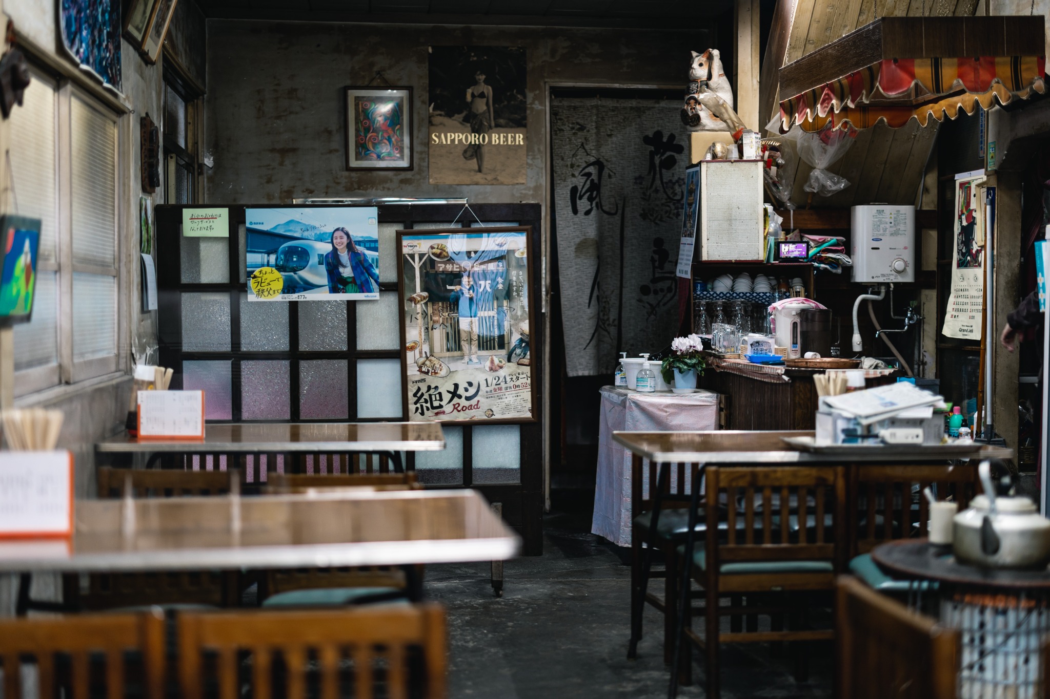 Interior of Pari Shokudo in Chichibu, with old tables and chairs, wall posters, shelves and a kettle resting on a stove.