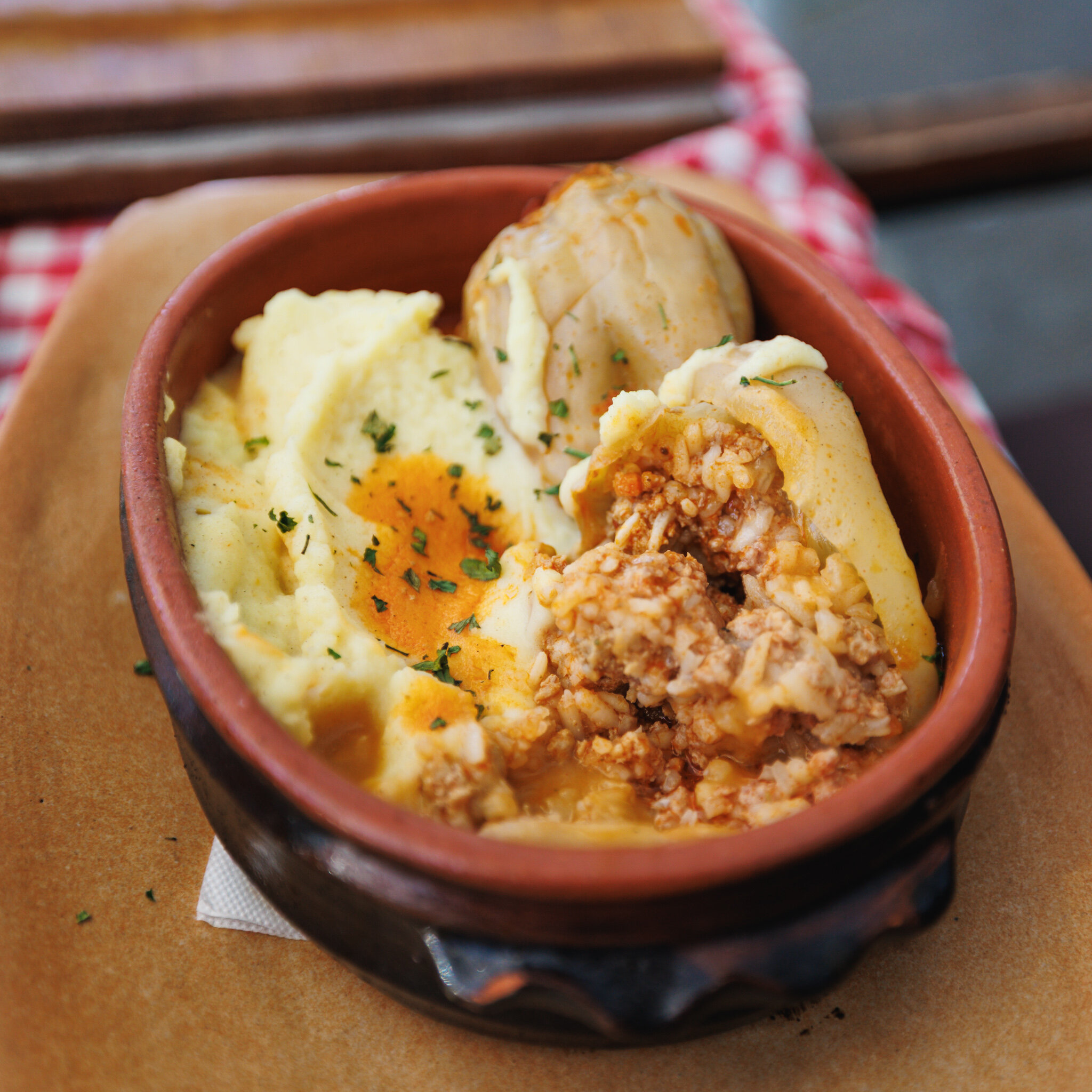 A cut-open stuffed pepper showing minced meat and rice beside mashed potatoes on an oval dish.