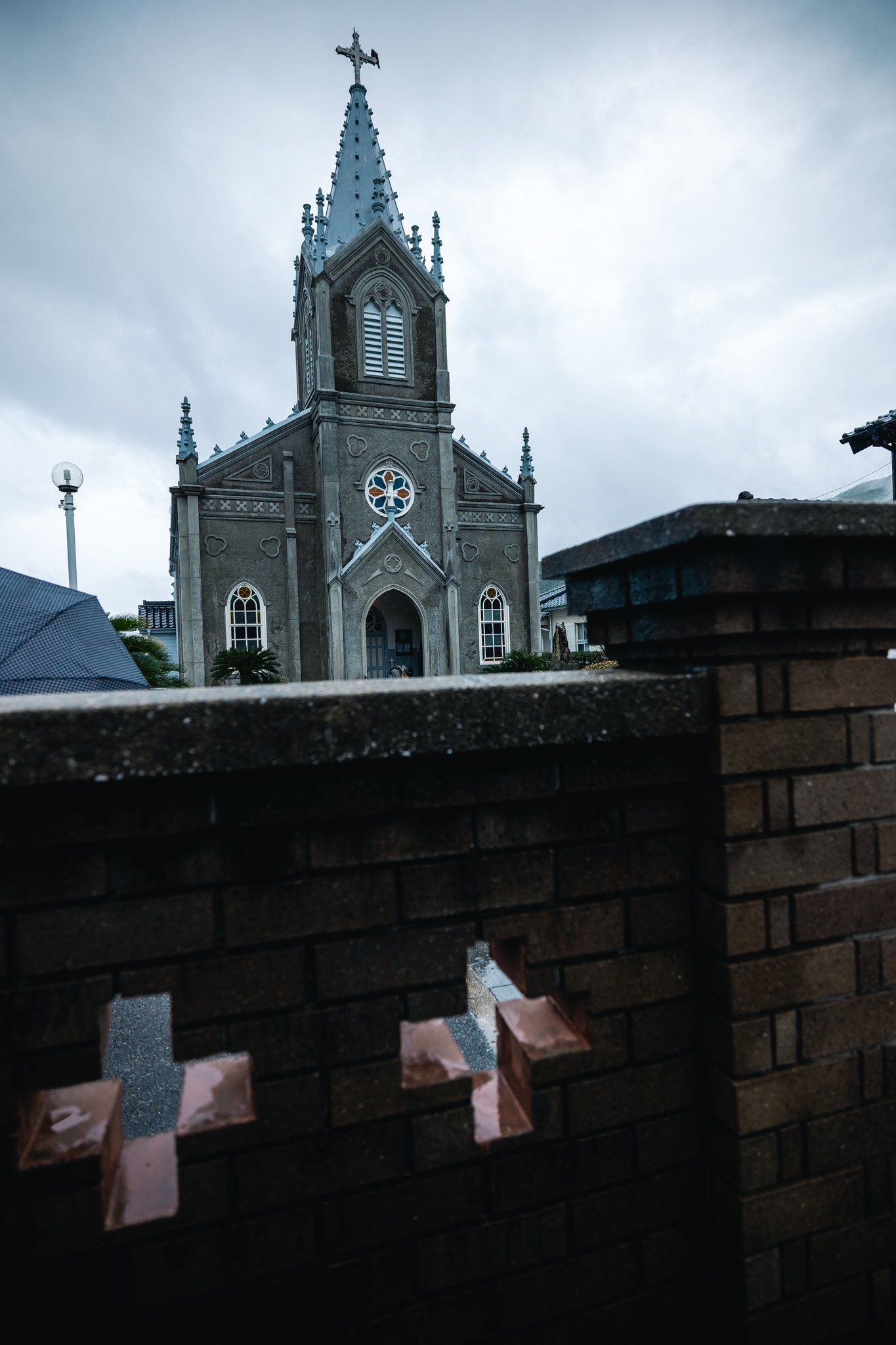 The grey Gothic front of Sakitsu Church seen over a brick wall with cross-shaped openings